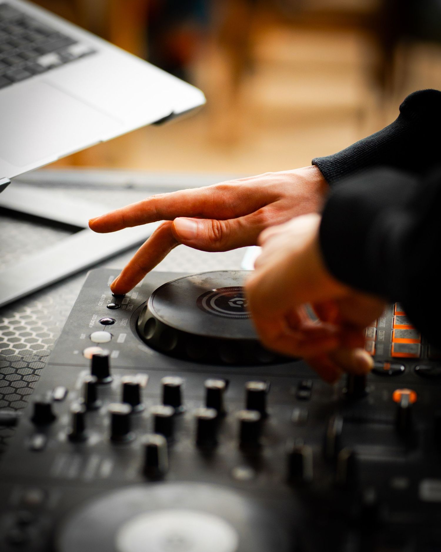 Close-up of a DJ's hand scratching a turntable on a professional DJ controller with knobs and faders.