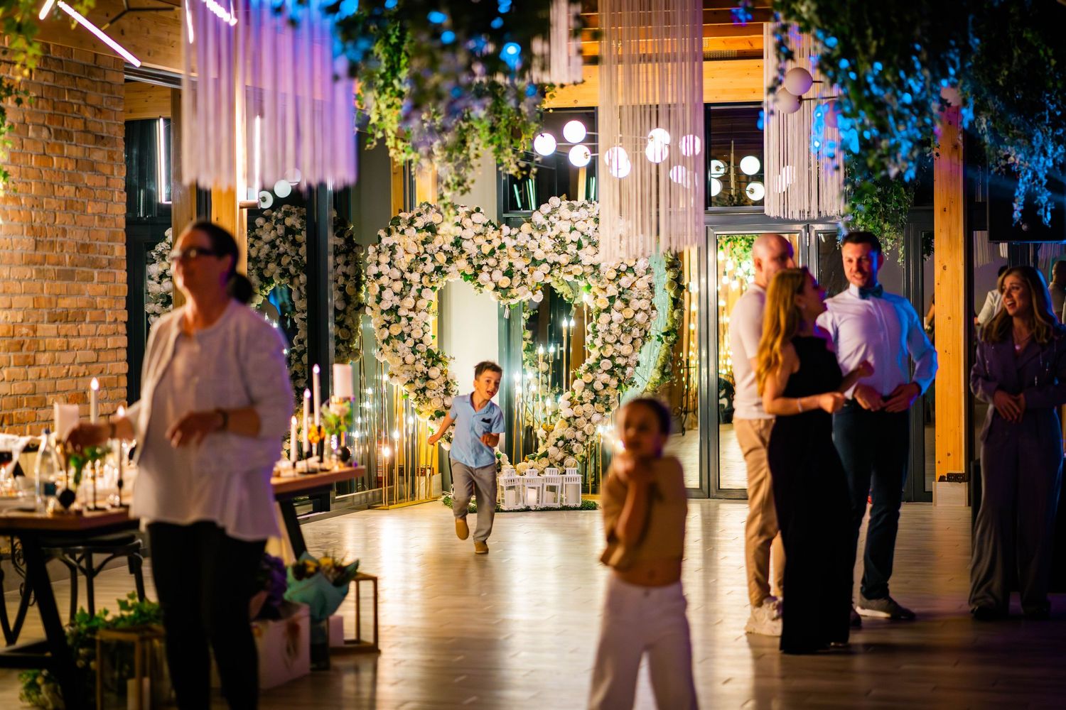 Invitati si copii la o petrecere de nunta seara cu decor floral iluminat