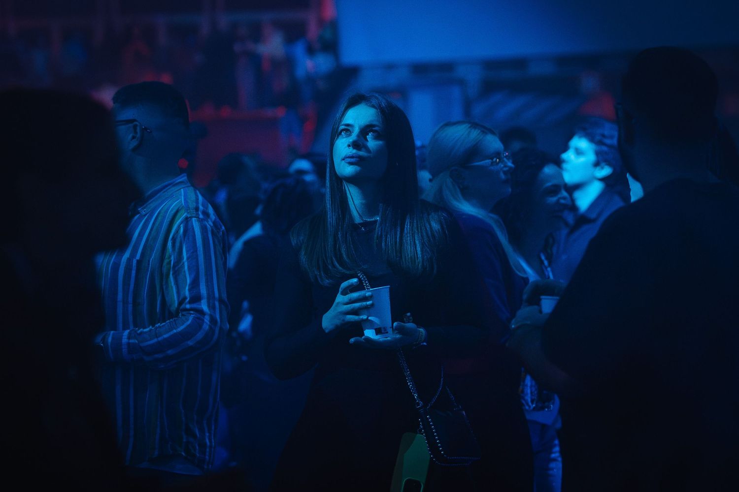 Tanara cu o bautura in mana privind spre scena in lumina albastra la un eveniment