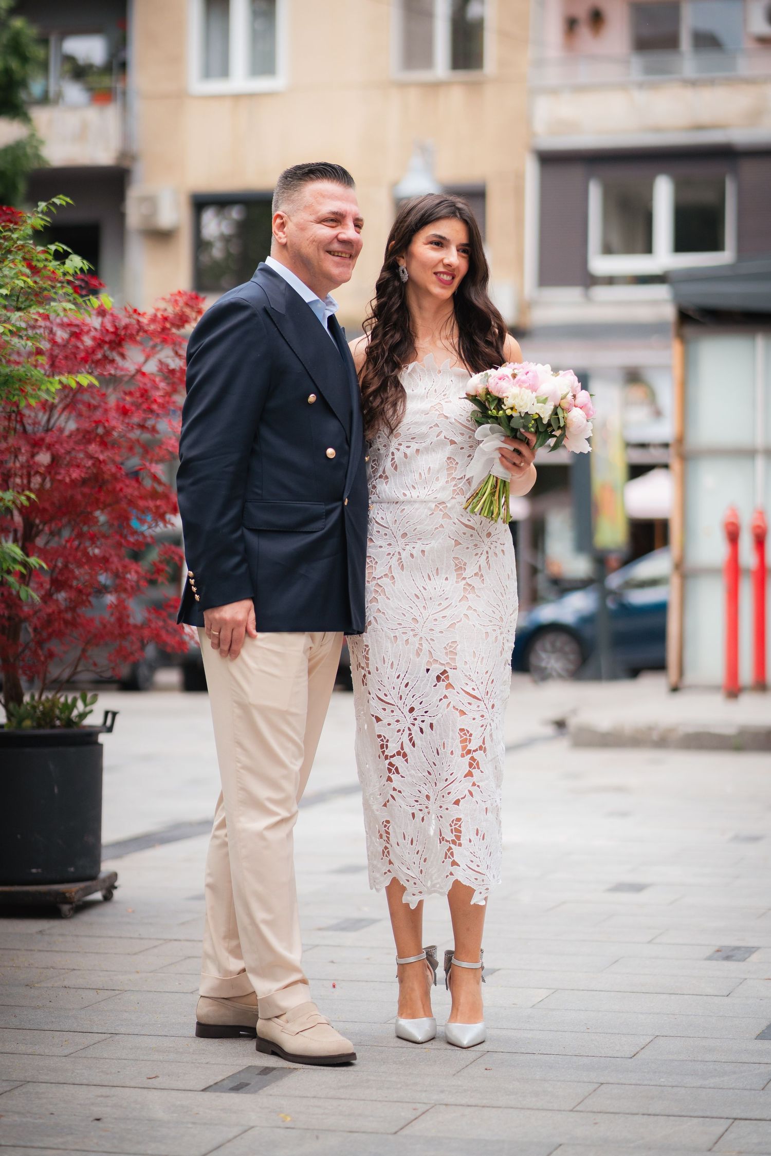 Mirii pozand pe o strada din oras, mireasa in rochie alba cu buchet de flori