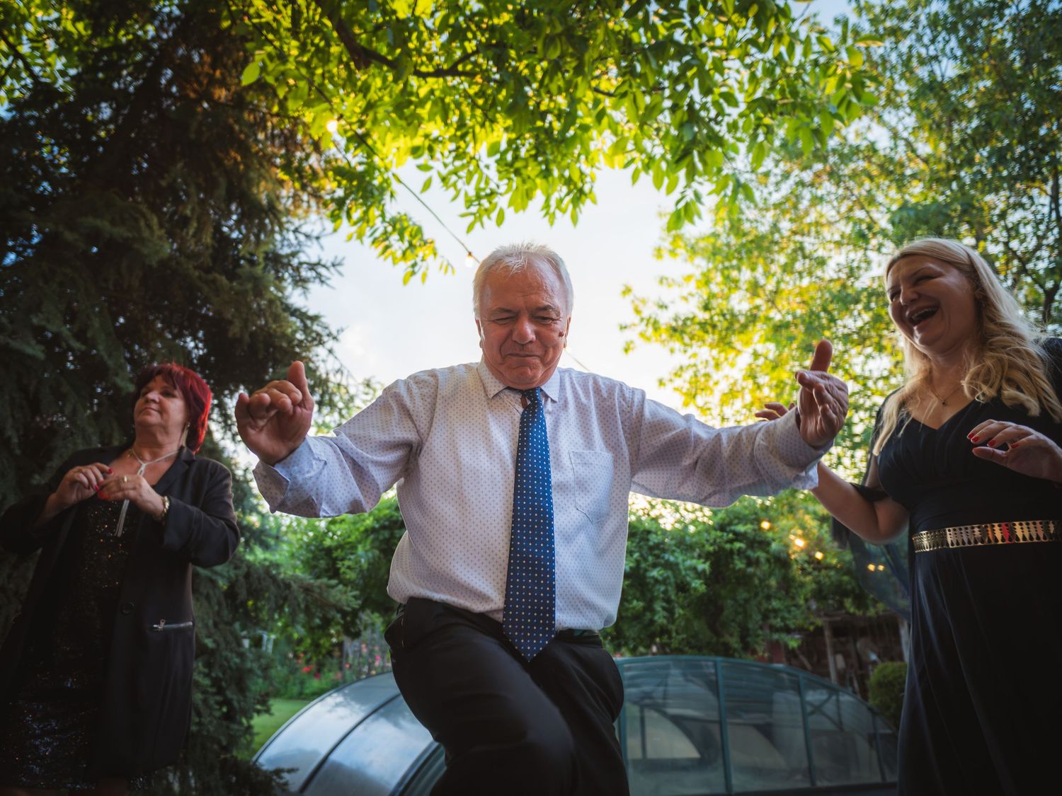 Bunic dansand bucuros cu invitatii la petrecerea in aer liber de dupa botez
