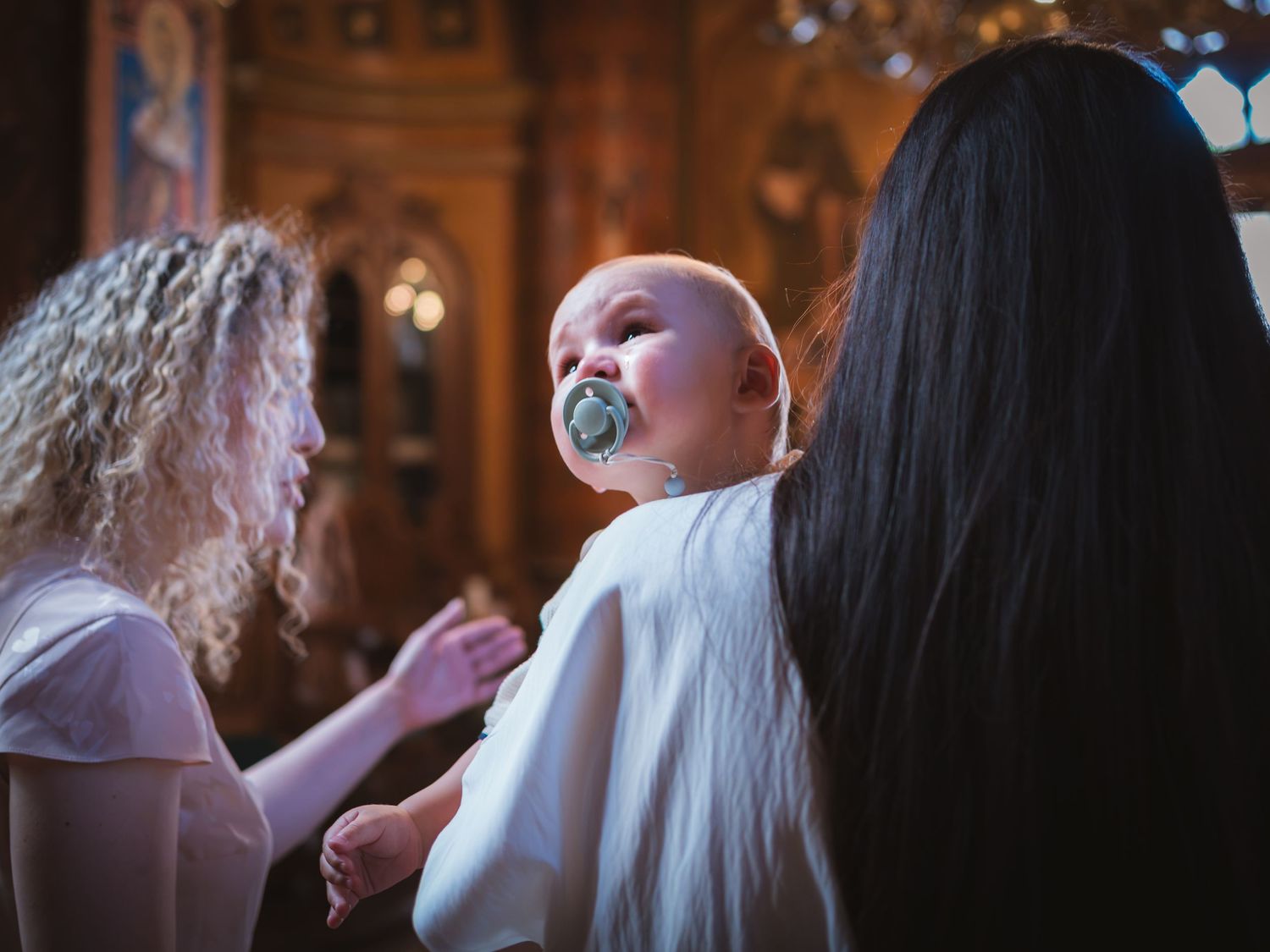 Mama tinand bebelusul in brate in biserica inainte de inceperea slujbei de botez