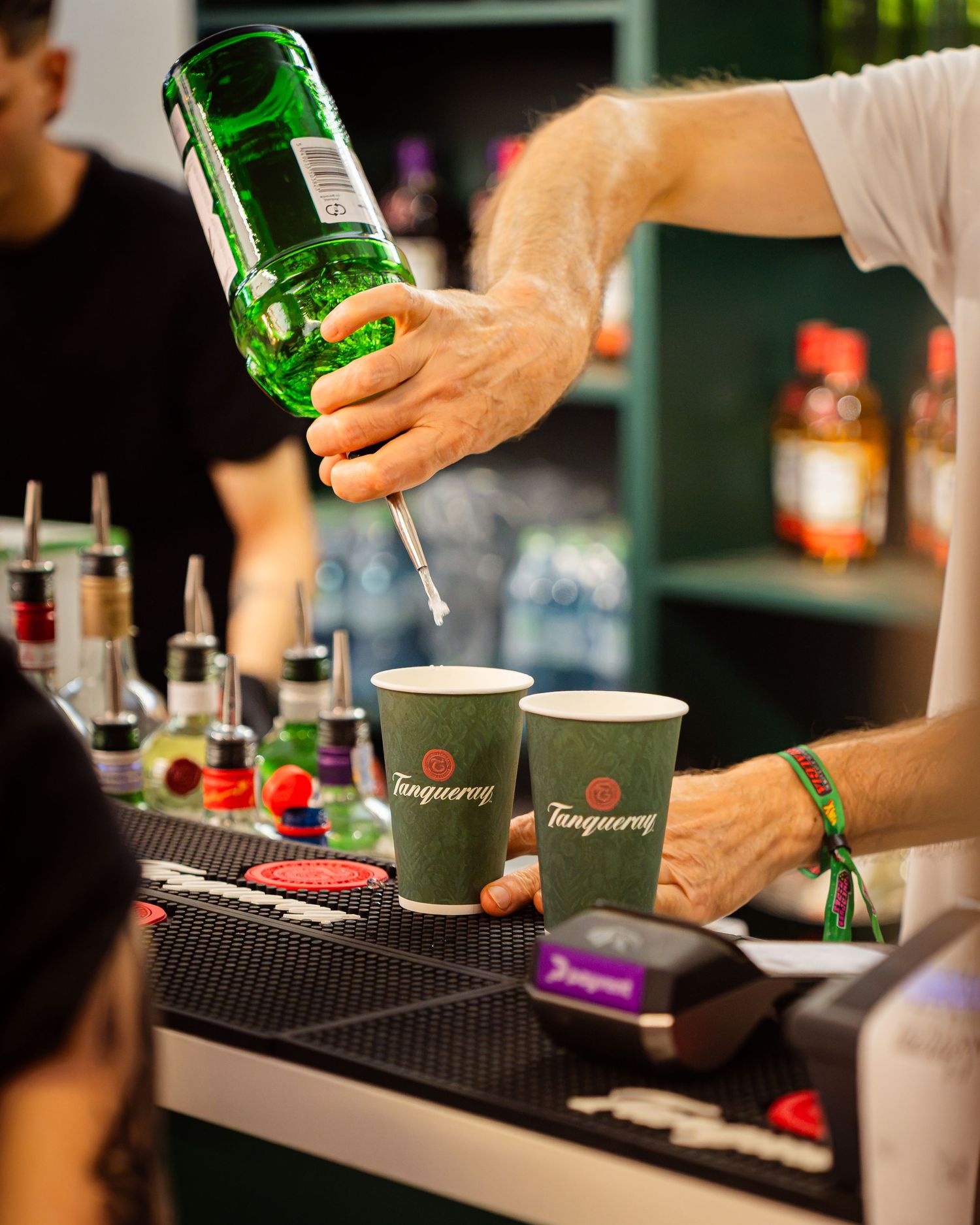 Barman turnand gin Tanqueray in pahare la barul unui festival in aer liber