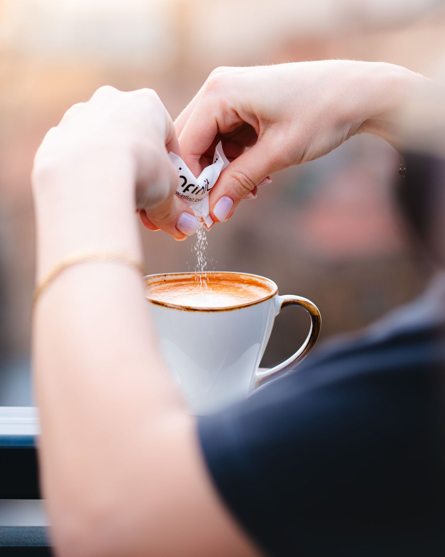 Detaliu cu maini turnand zahar intr-o ceasca de cappuccino, fotografie comerciala pentru cafenele