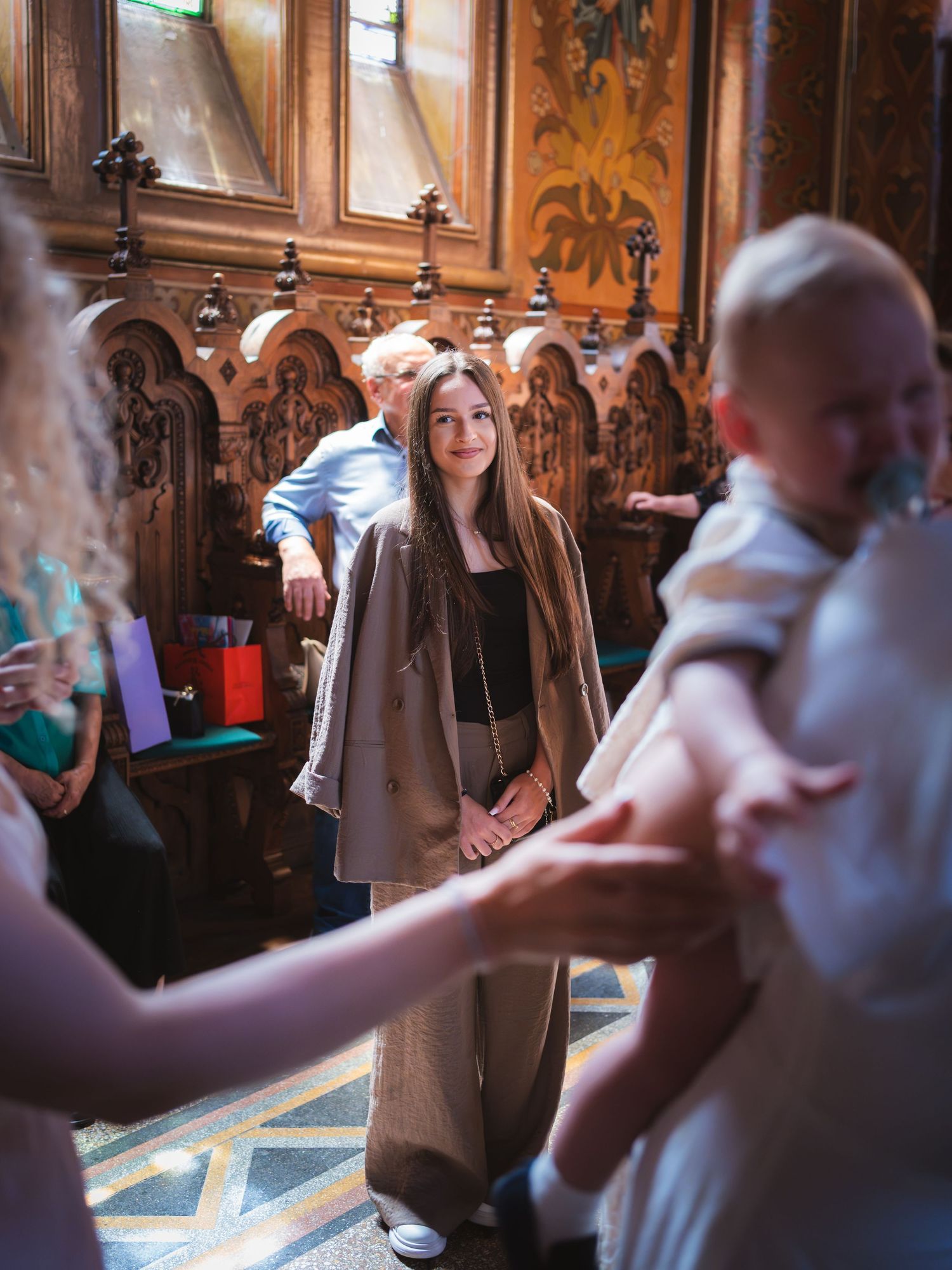 Tanara in sacou bej alaturi de familie in biserica la ceremonia de botez
