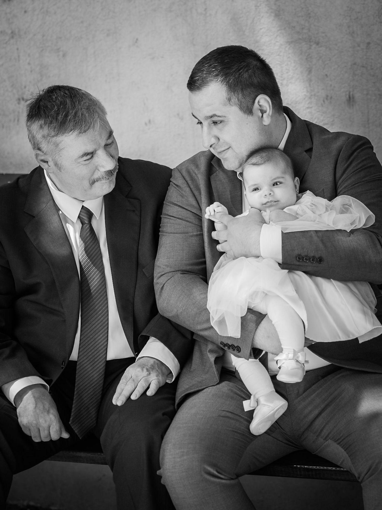Portret alb-negru de familie cu bunicul, tatal si bebelusul imbracati elegant la botez