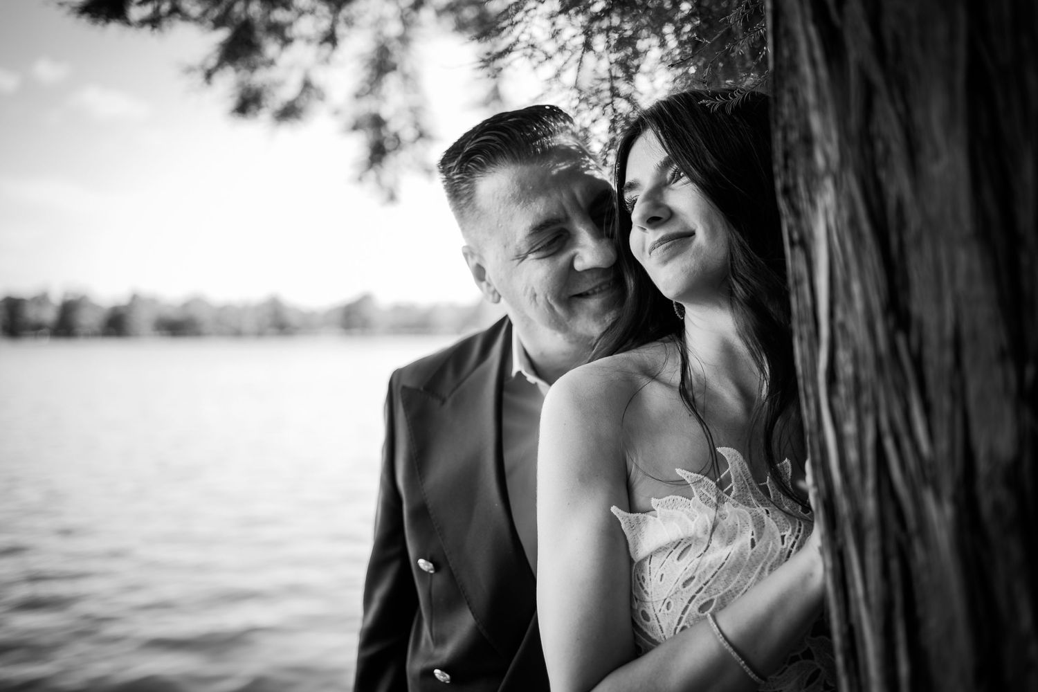 Portret alb-negru romantic cu mirii langa un copac pe malul lacului