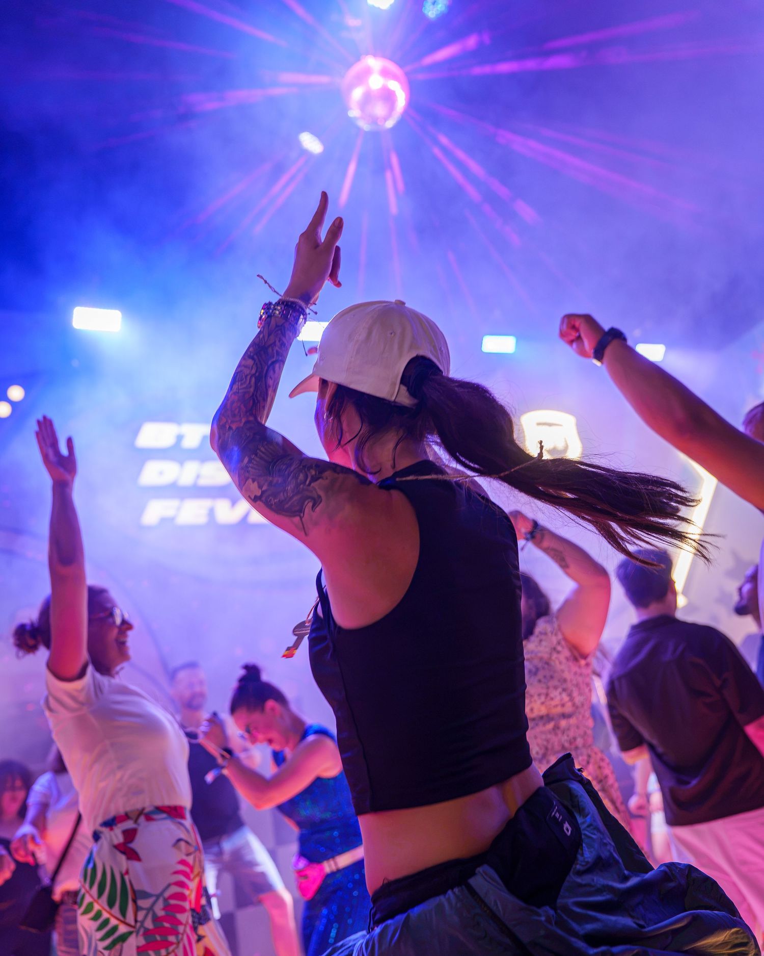 Tanara cu sapca alba dansand sub globul disco la un festival de muzica