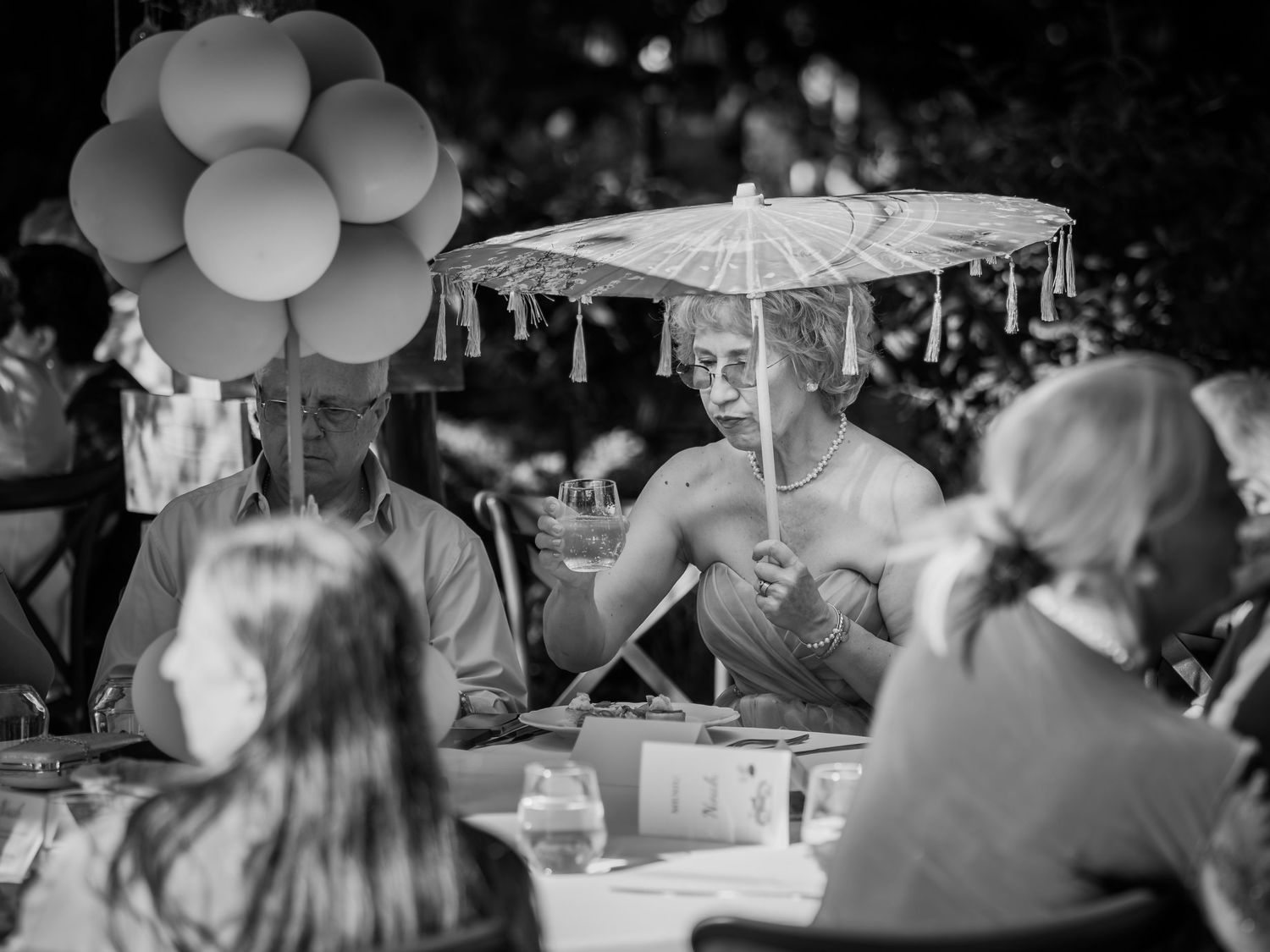 Foto alb-negru cu invitati la masa de botez in aer liber cu baloane decorative