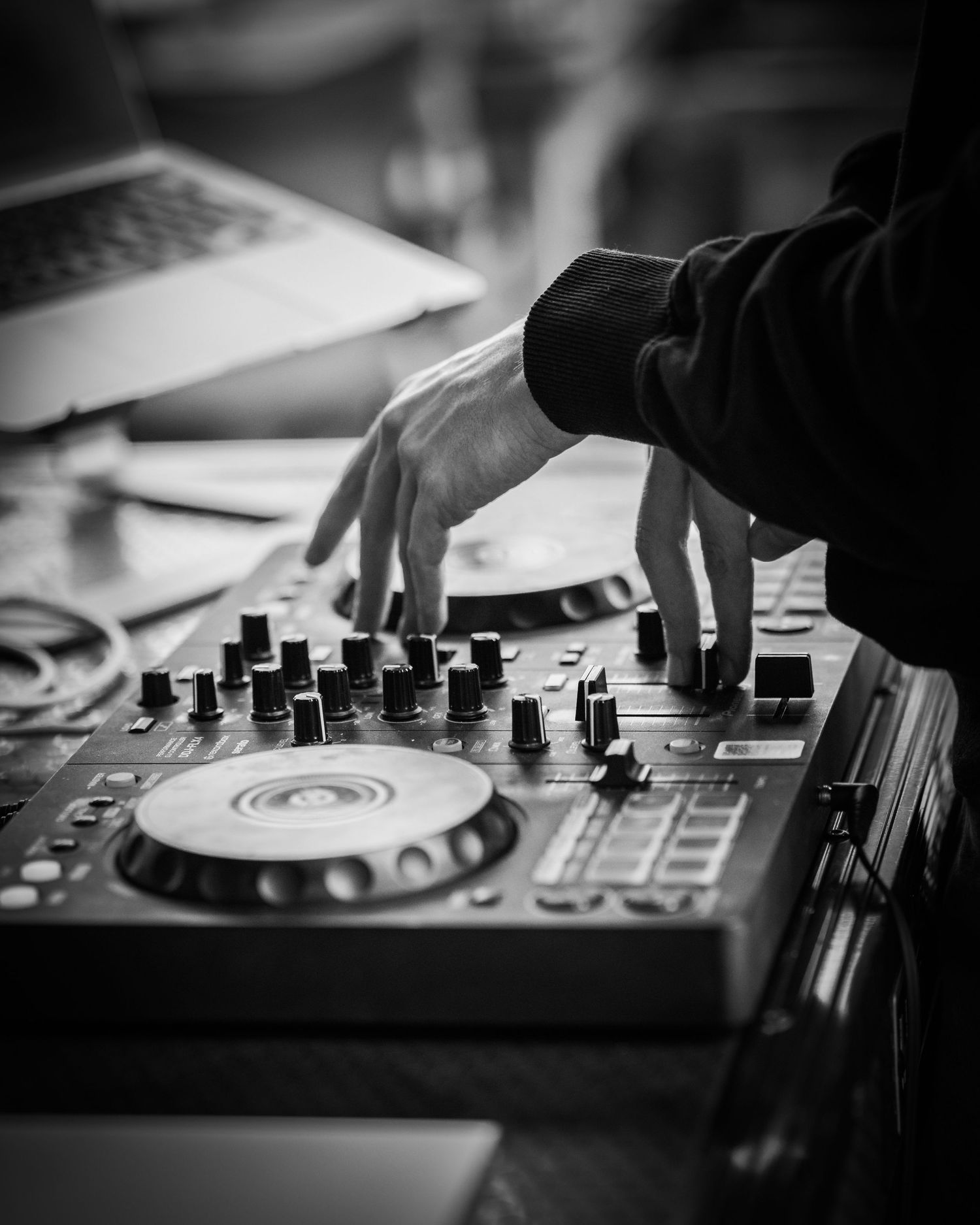 Foto alb-negru cu un DJ care mixeaza pe o consola la un eveniment privat
