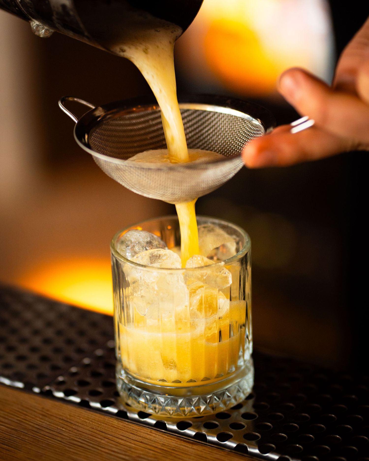 Barman preparand un cocktail auriu intr-un pahar cu gheata, fotografie comerciala pentru baruri