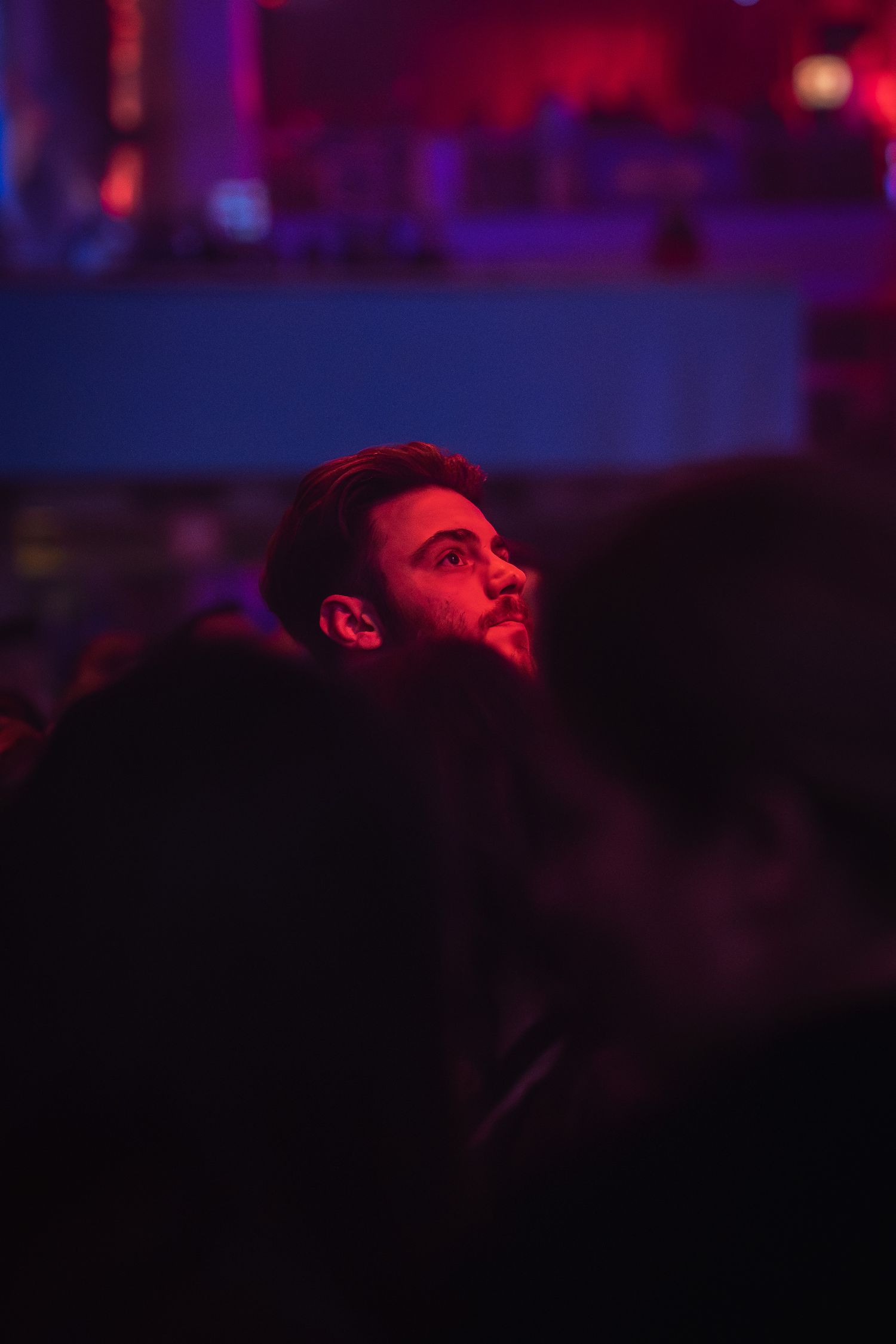 Tanar privind spre scena in lumina rosie de neon la un concert