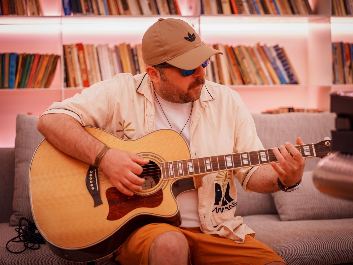 Muzician cantand la chitara acustica pe canapea intr-un studio muzical