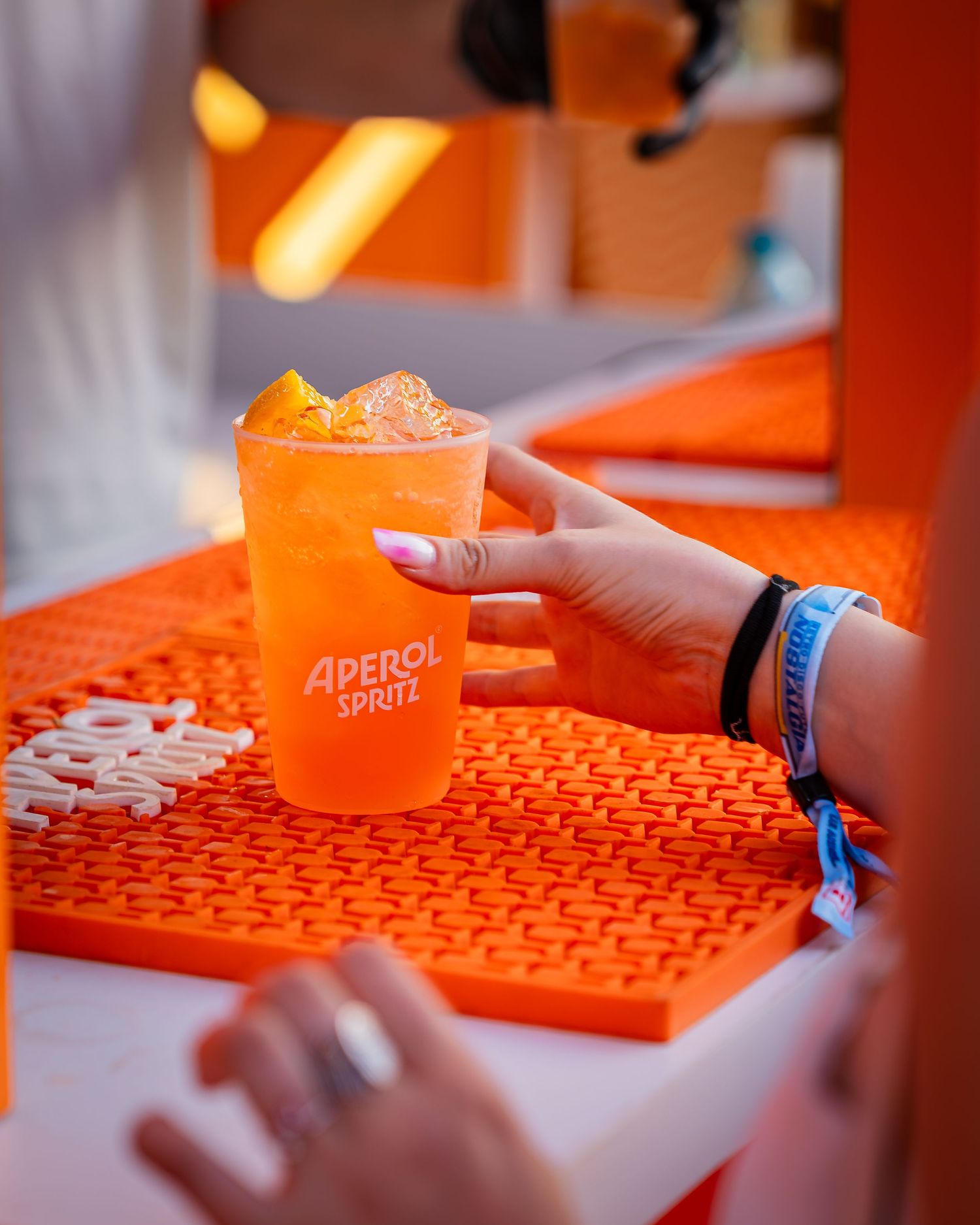 Mana tinand un pahar de cocktail Aperol Spritz la tejgheaua unui bar de festival