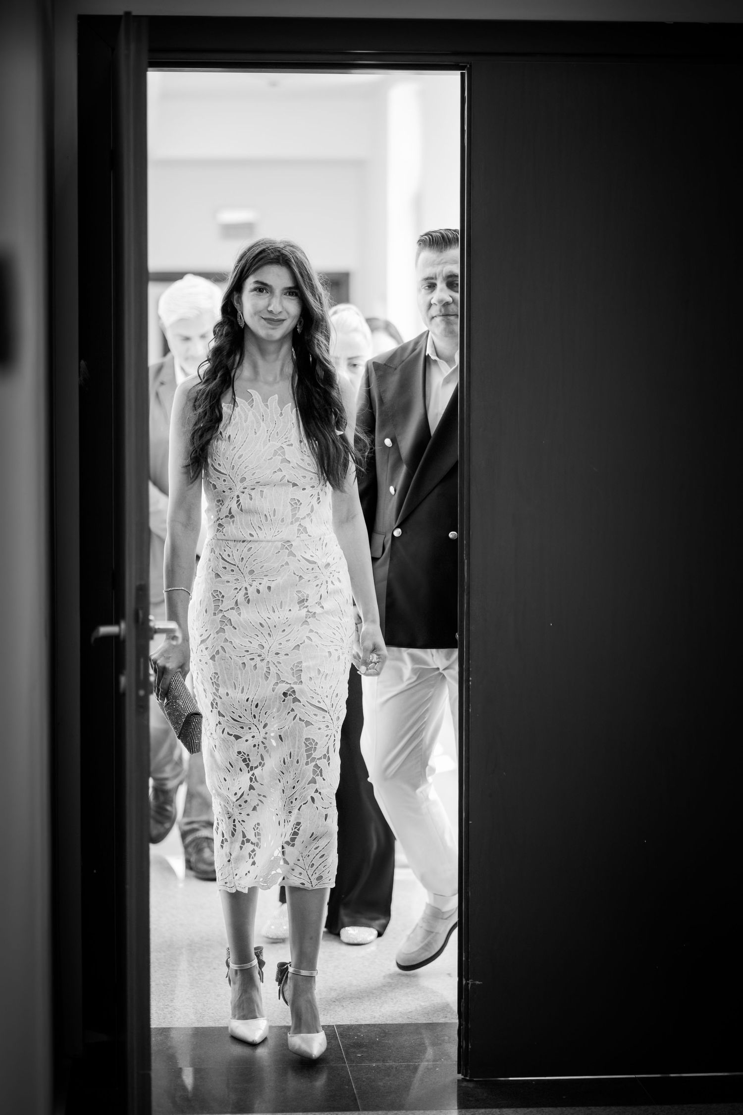 Mireasa eleganta in rochie alba intrand pe usa alaturi de mire, fotografie alb-negru