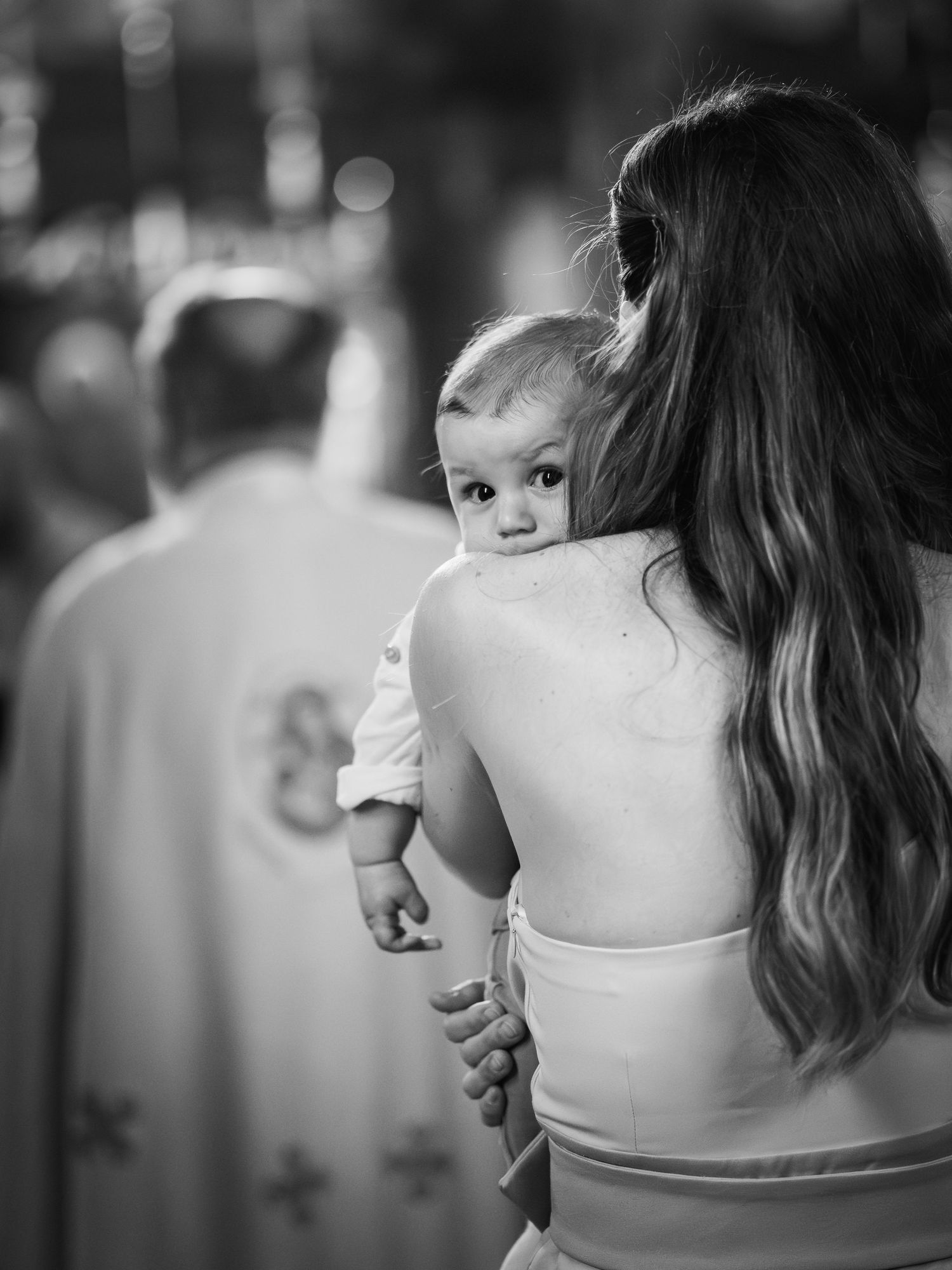 Foto alb-negru cu mama tinand copilul in brate in timpul botezului ortodox