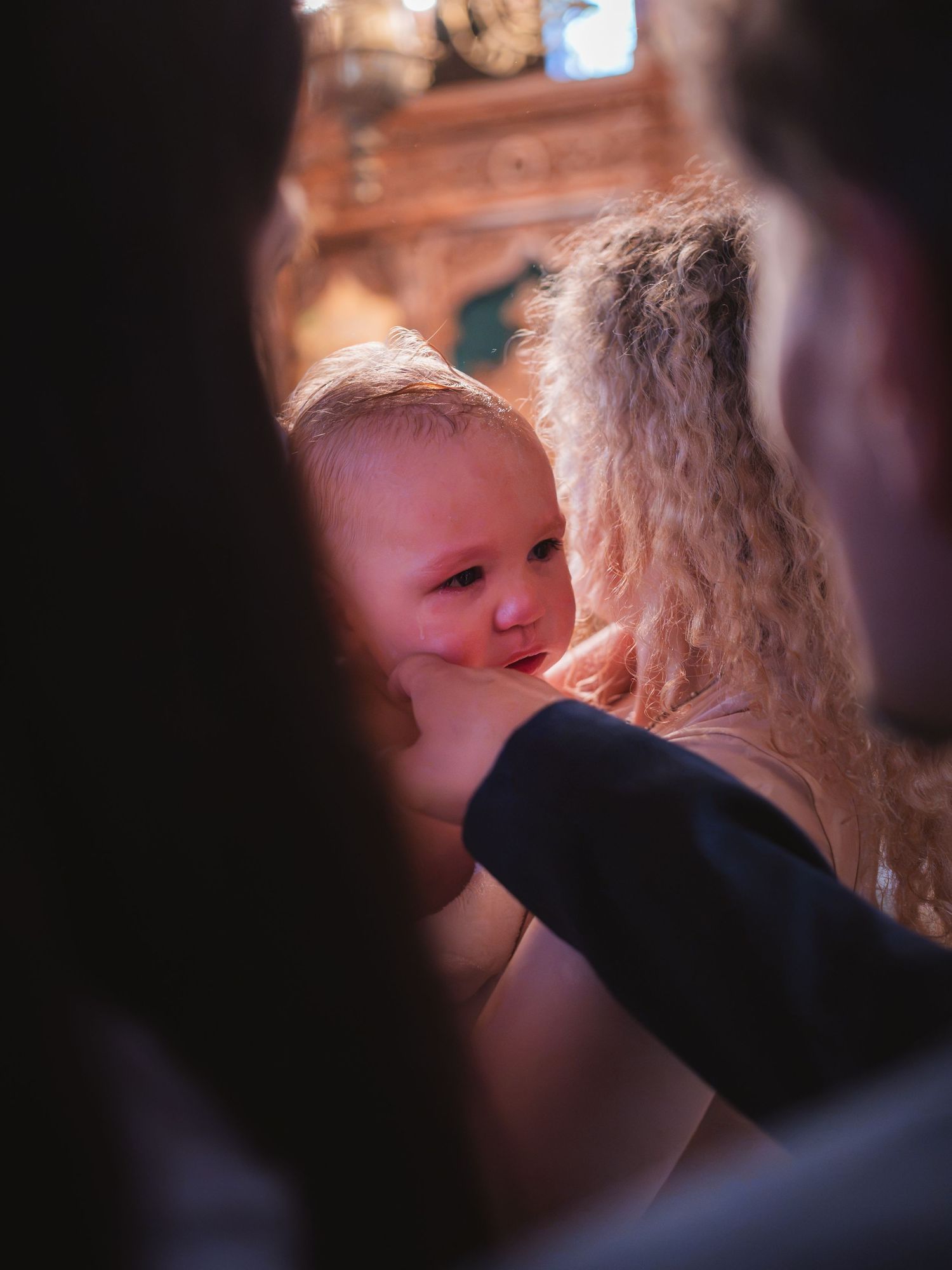 Femeie tinand in brate un bebelus emotionat in timpul ceremoniei de botez din biserica