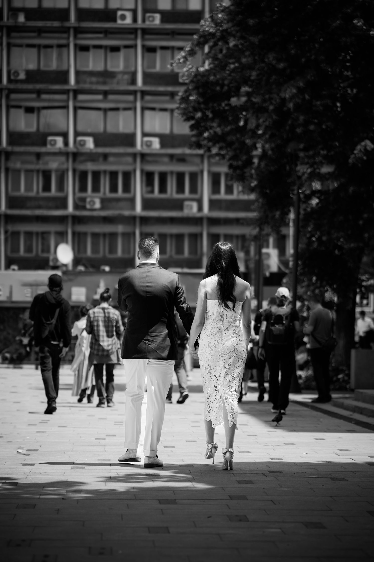 Foto alb-negru cu mirii plimbandu-se impreuna printr-o piata publica din oras