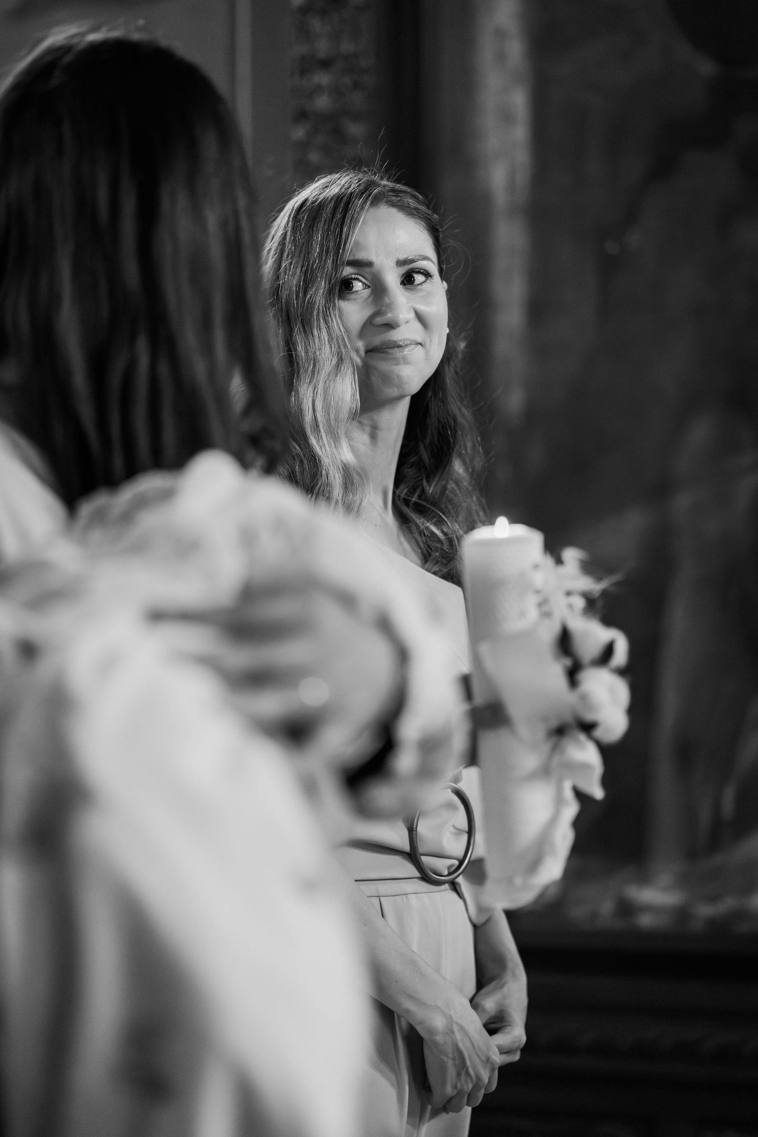 Black and white photo of a woman holding a candle at a church ceremony, gazing upward with a serene expression.