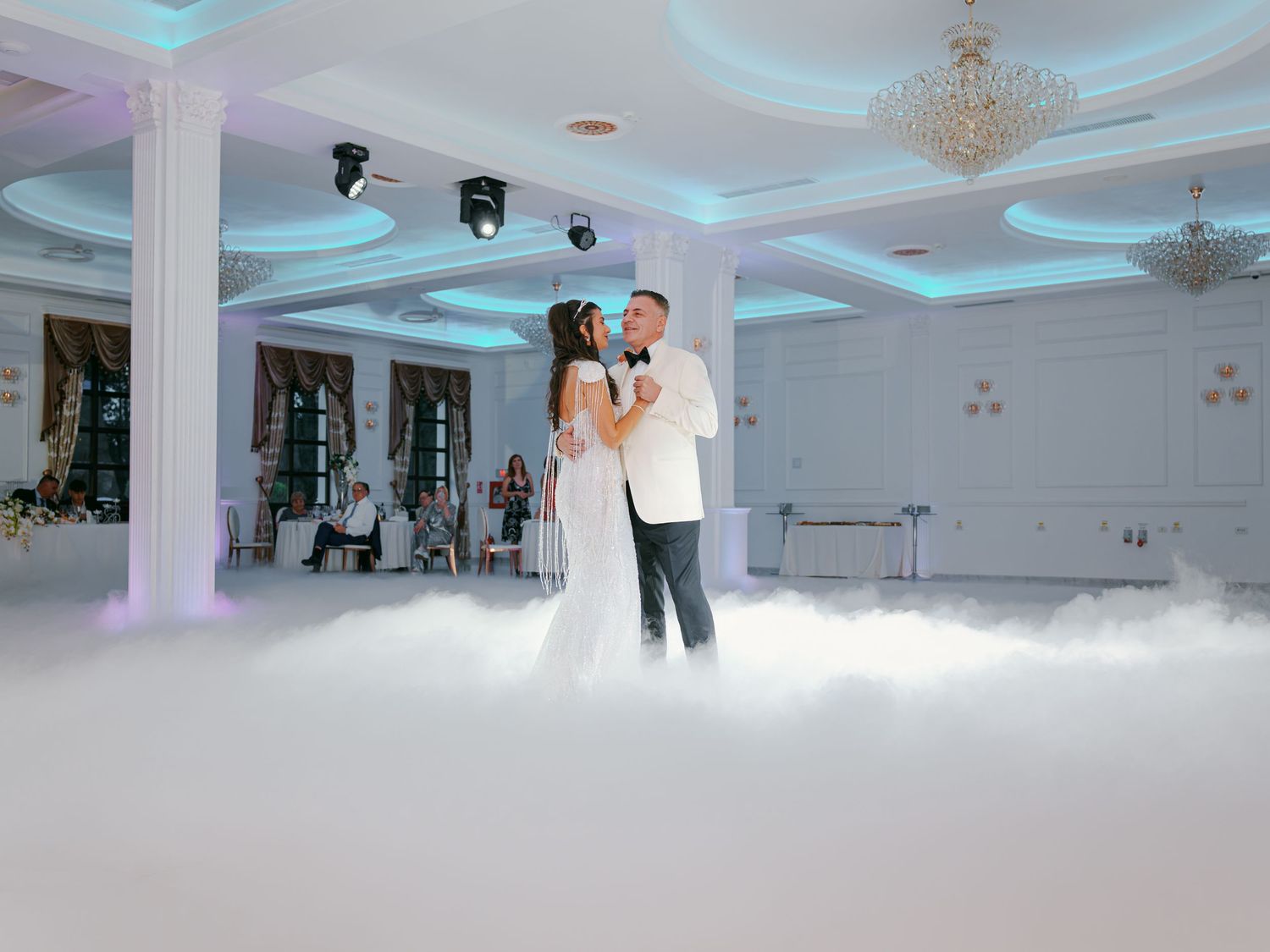 Bride and groom share first dance on a cloud-filled wedding reception floor in an elegant white ballroom.