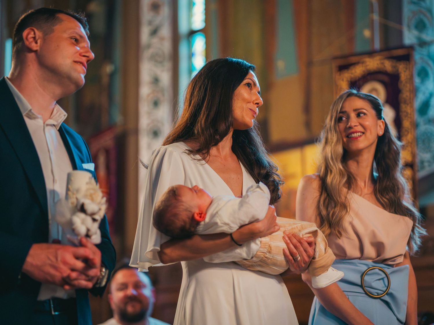Parintii si nasa tinand bebelusul in brate in timpul slujbei de botez la biserica