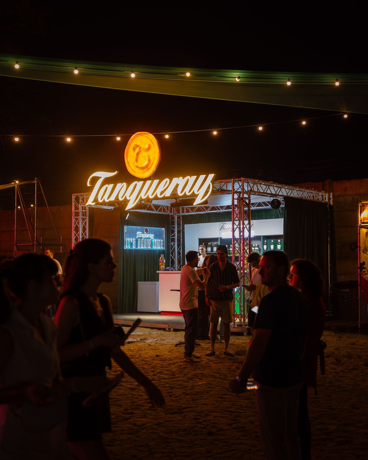 Tanqueray intrare iluminata la un stand de brand in timpul unui festival de muzica noaptea.
