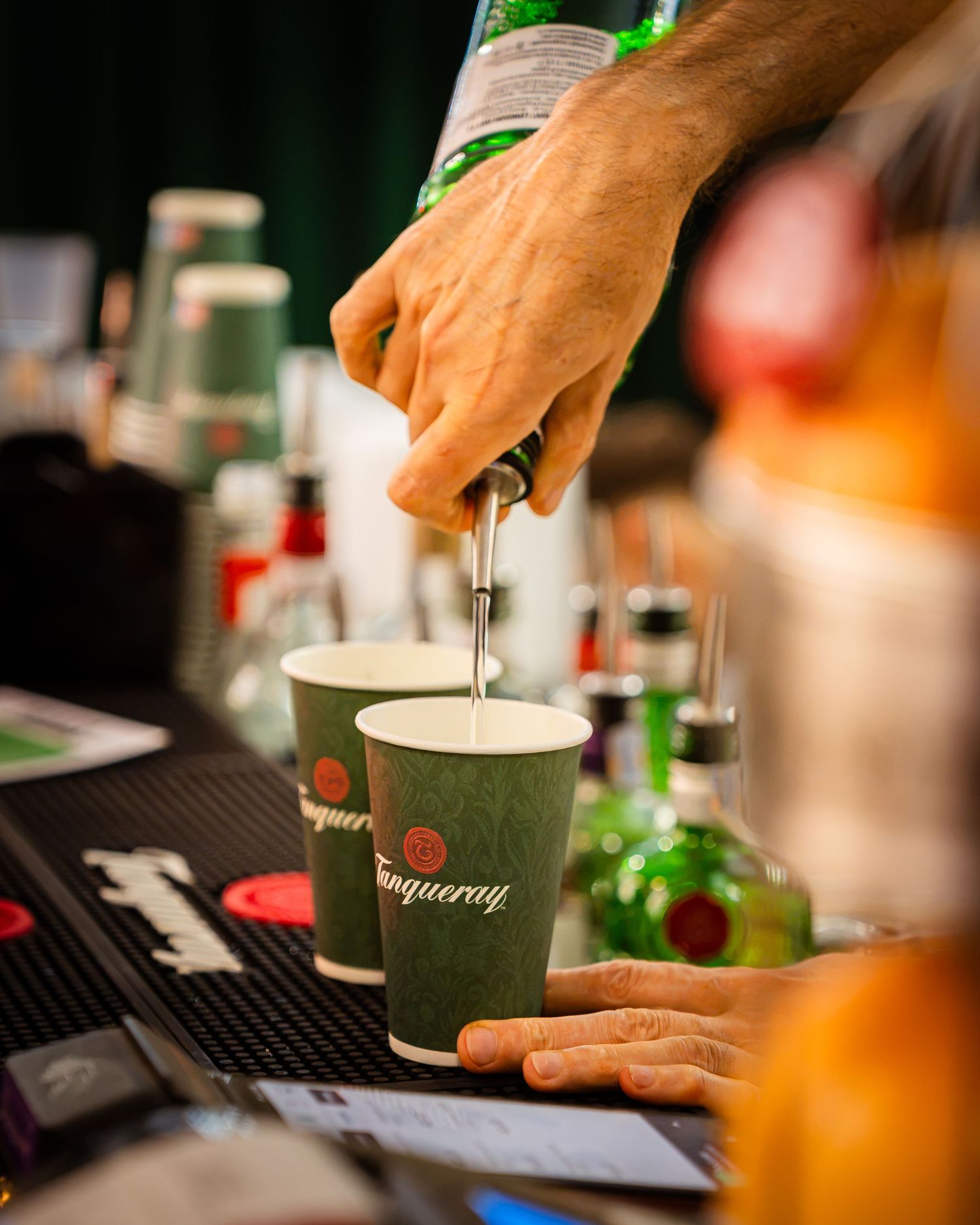 Barman pregatind cocktailuri in pahare verzi Tanqueray la un bar de festival