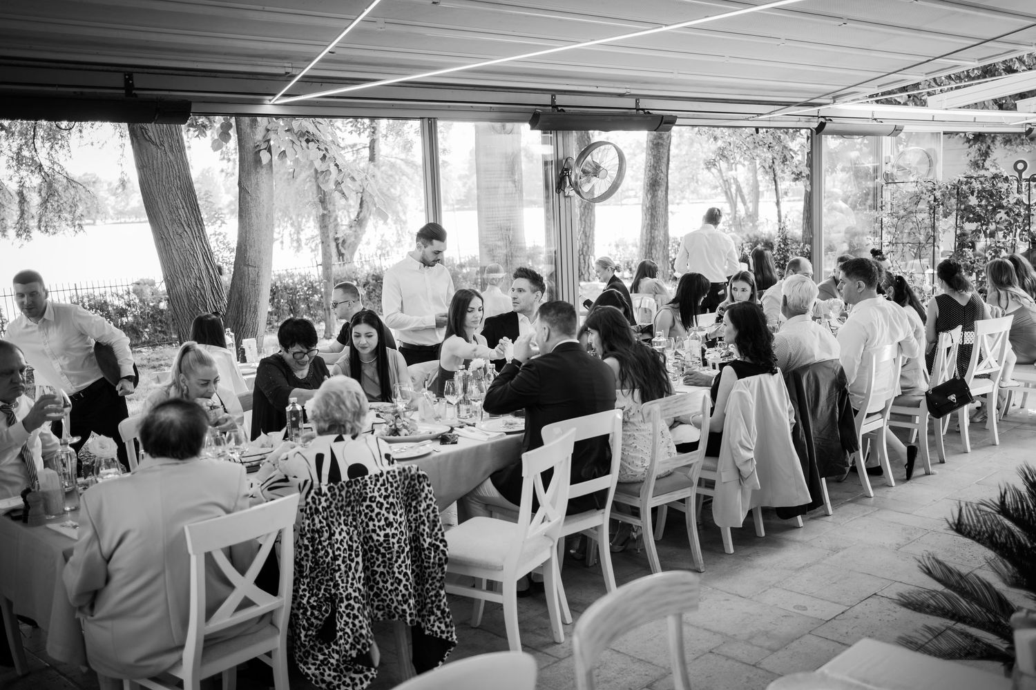 Black and white aerial view of wedding reception guests dining at long tables under outdoor canopy.