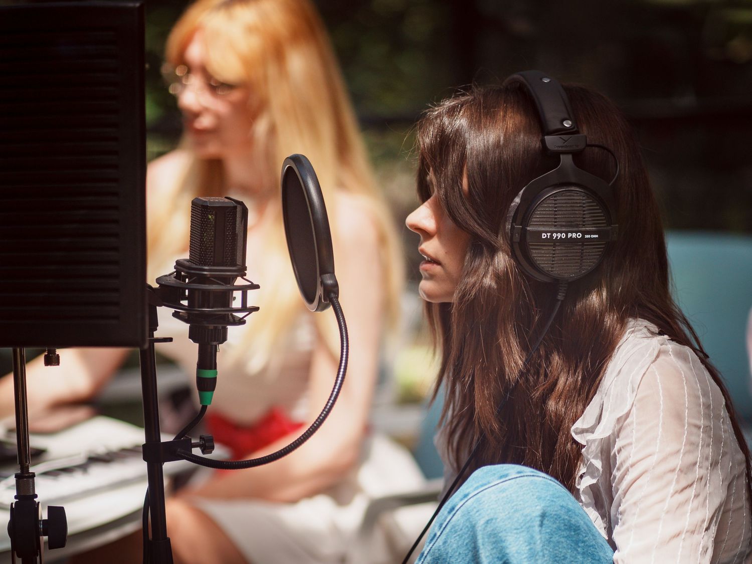 Woman wearing headphones recording vocals at a studio microphone with pop filter outdoors.