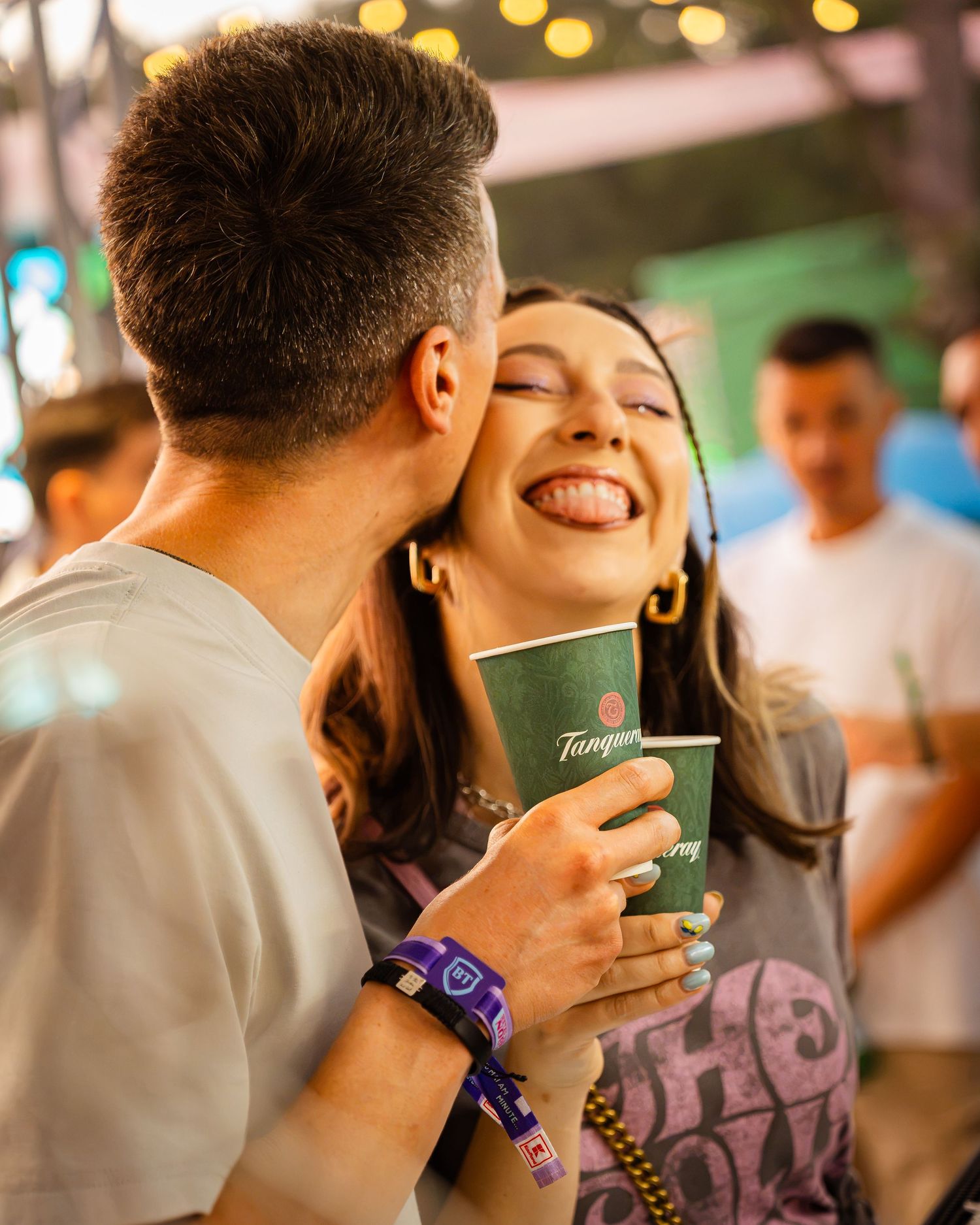 Tanara razand fericita in timp ce este sarutata pe obraz la un festival, cadru candid