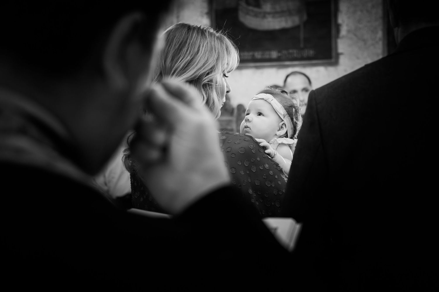 Portret alb-negru cu o femeie tinand bebelusul in brate in timpul slujbei de botez