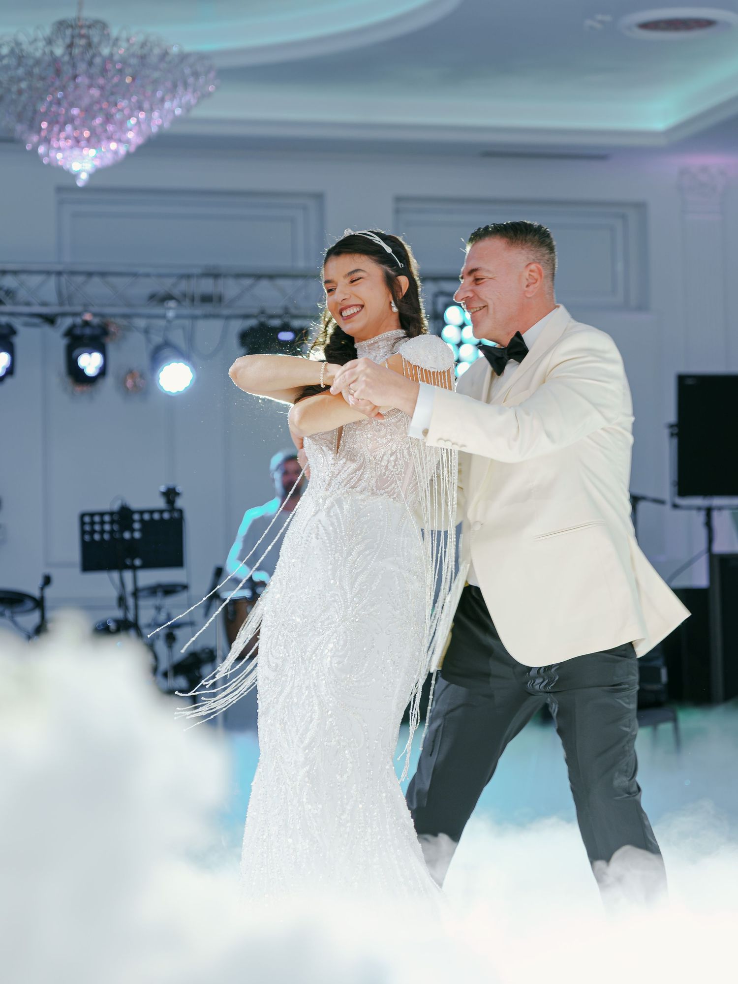 Bride and groom share their first dance on a cloud-filled floor in an elegant ballroom with crystal chandeliers.