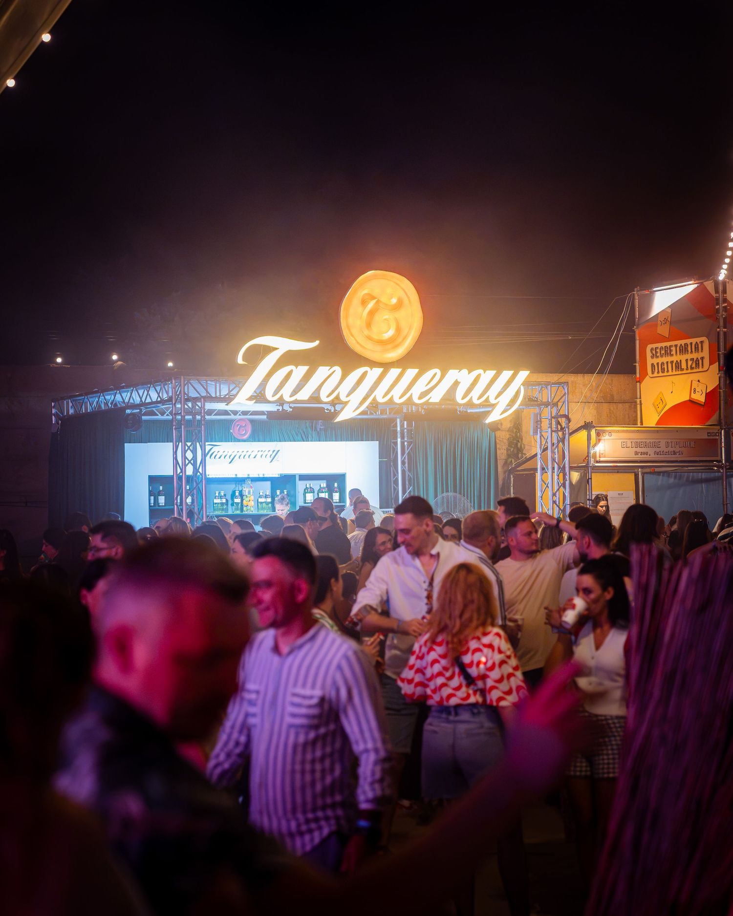 Multime bucurandu-se de un festival pe timp de noapte sub un semn luminos Tanqueray