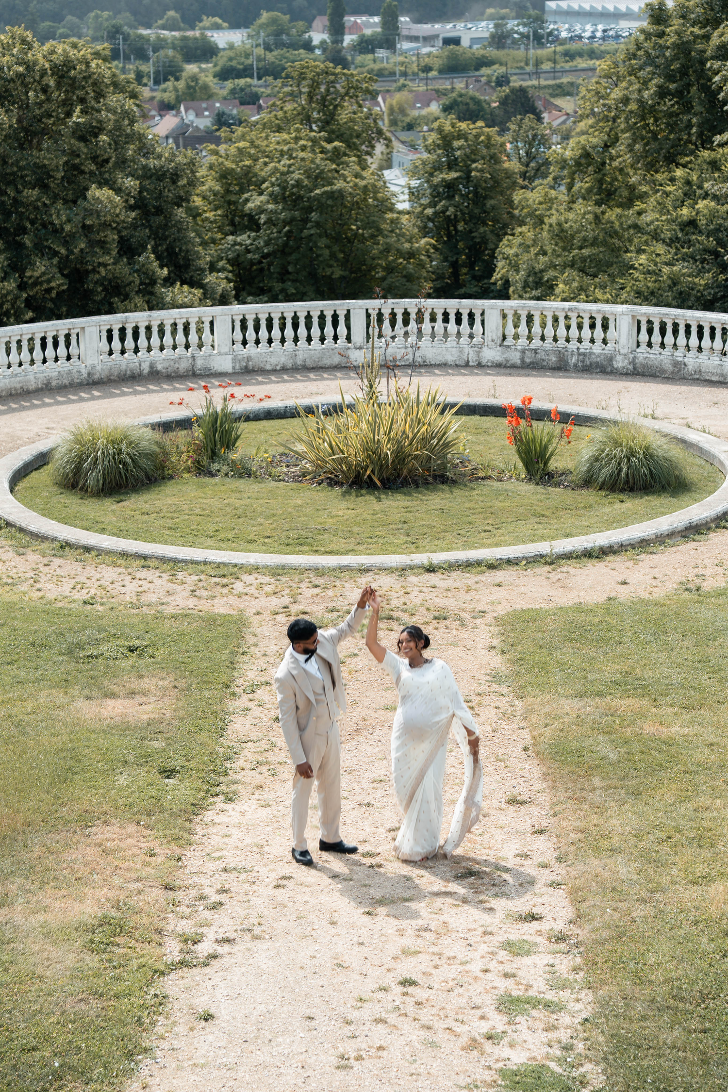Vue en hauteur d’un couple de mariés dansant dans les jardins de leur lieu de réception.