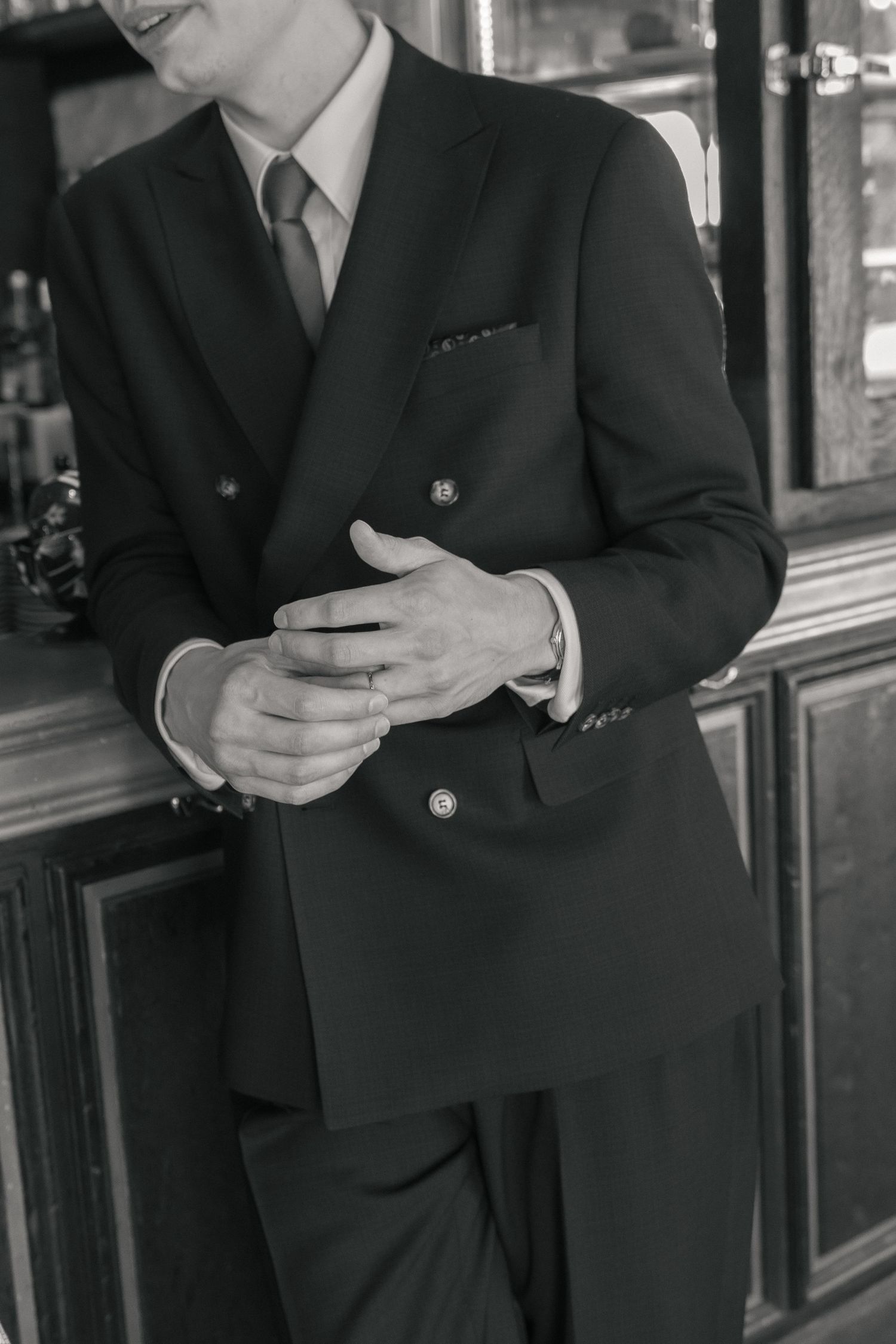 Détail du costume croisé et des mains du marié, photographié en noir et blanc.