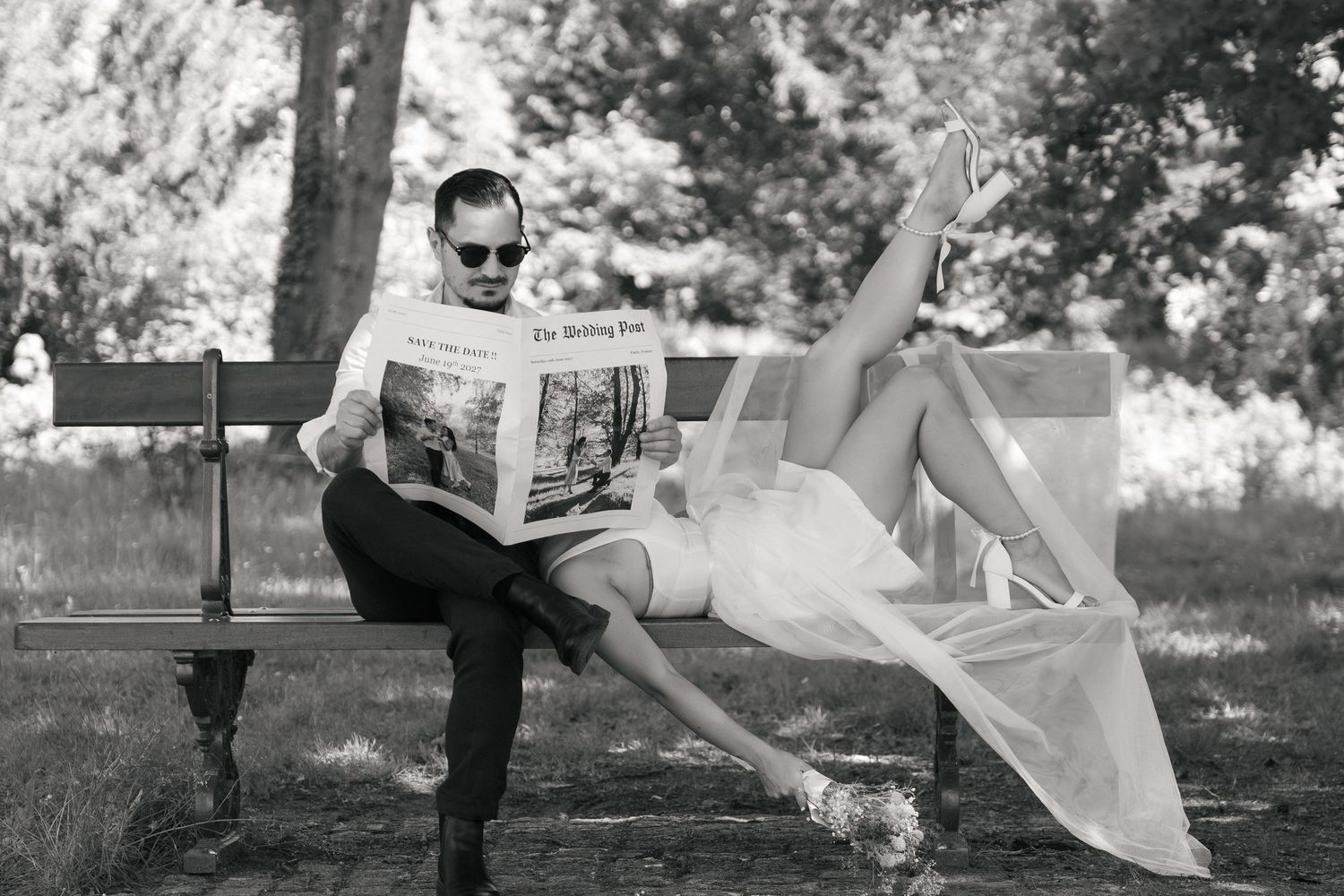 Couple assis sur un banc avec son faire-part au format journal lors d’une séance de fiançailles en extérieur.