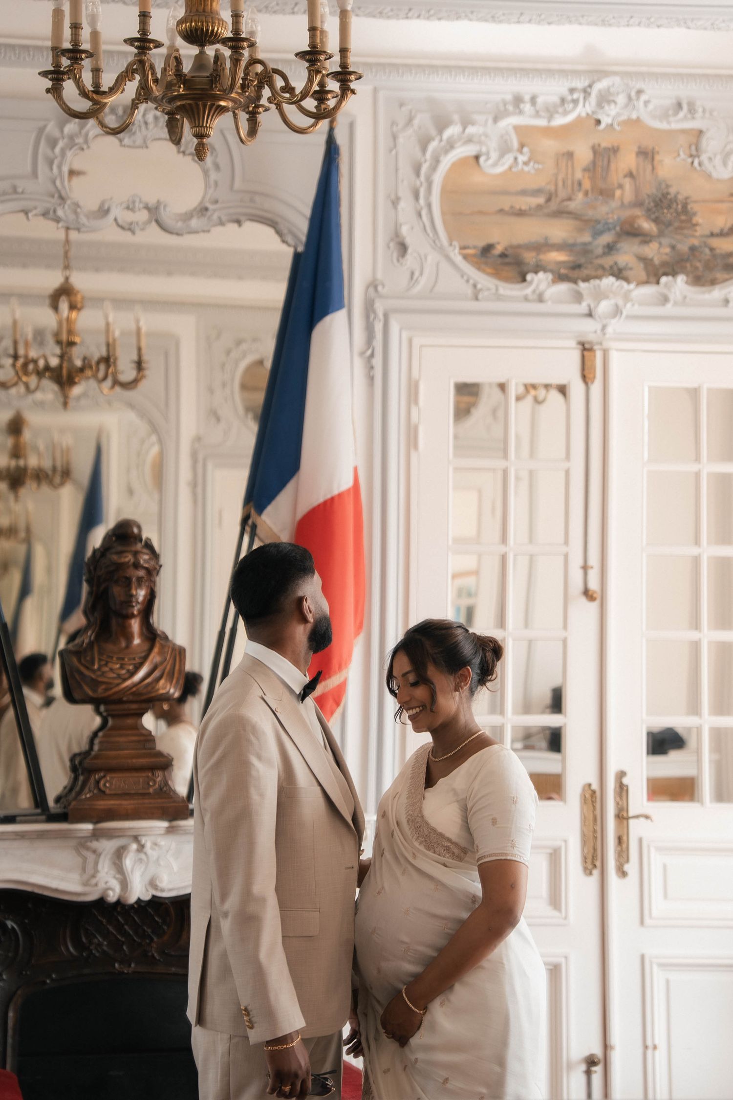 Mariés se regardant dans une salle de mairie élégante, près du drapeau français.