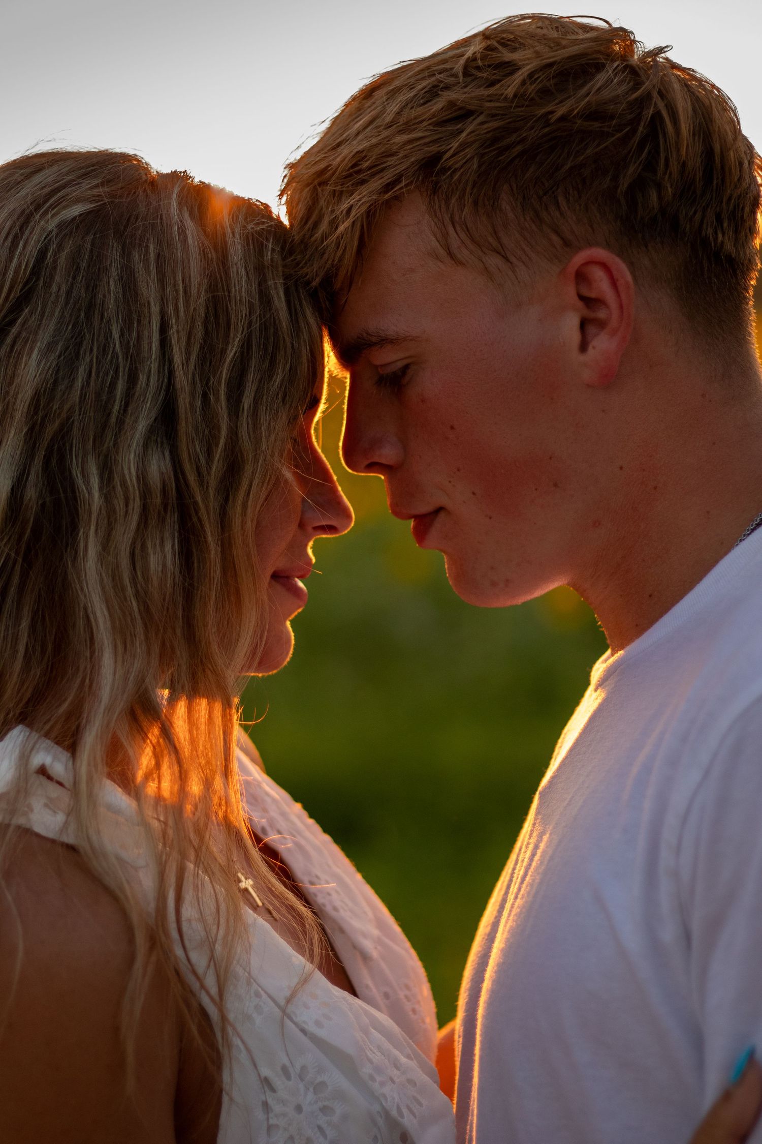 Romantic young couple touching foreheads in golden sunset light outdoors.