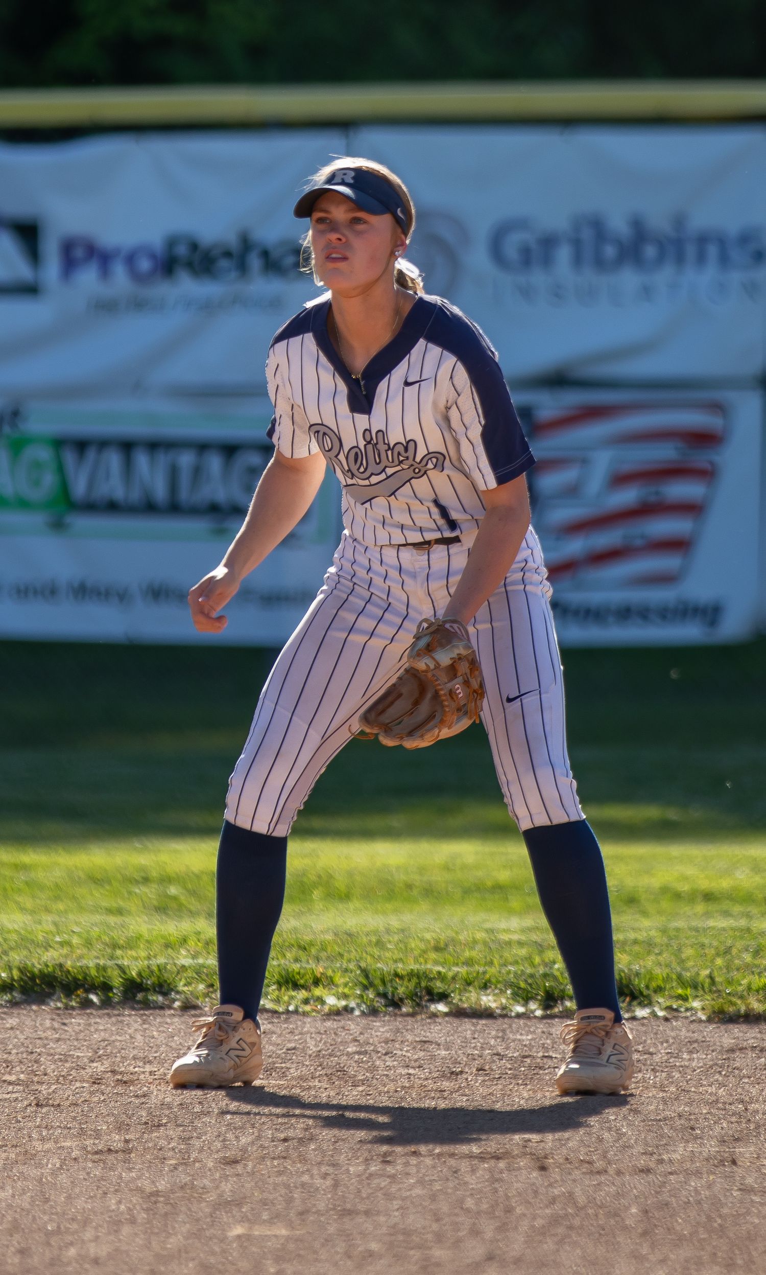 Ruffner softball infielder in pinstripe uniform stands ready in fielding position on the diamond.