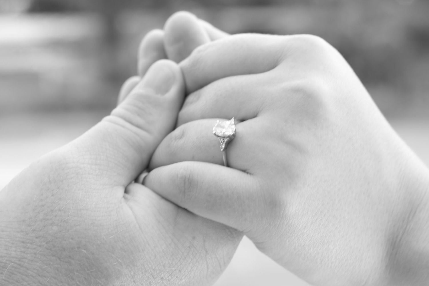 Black and white close-up of couple holding hands with diamond engagement ring.
