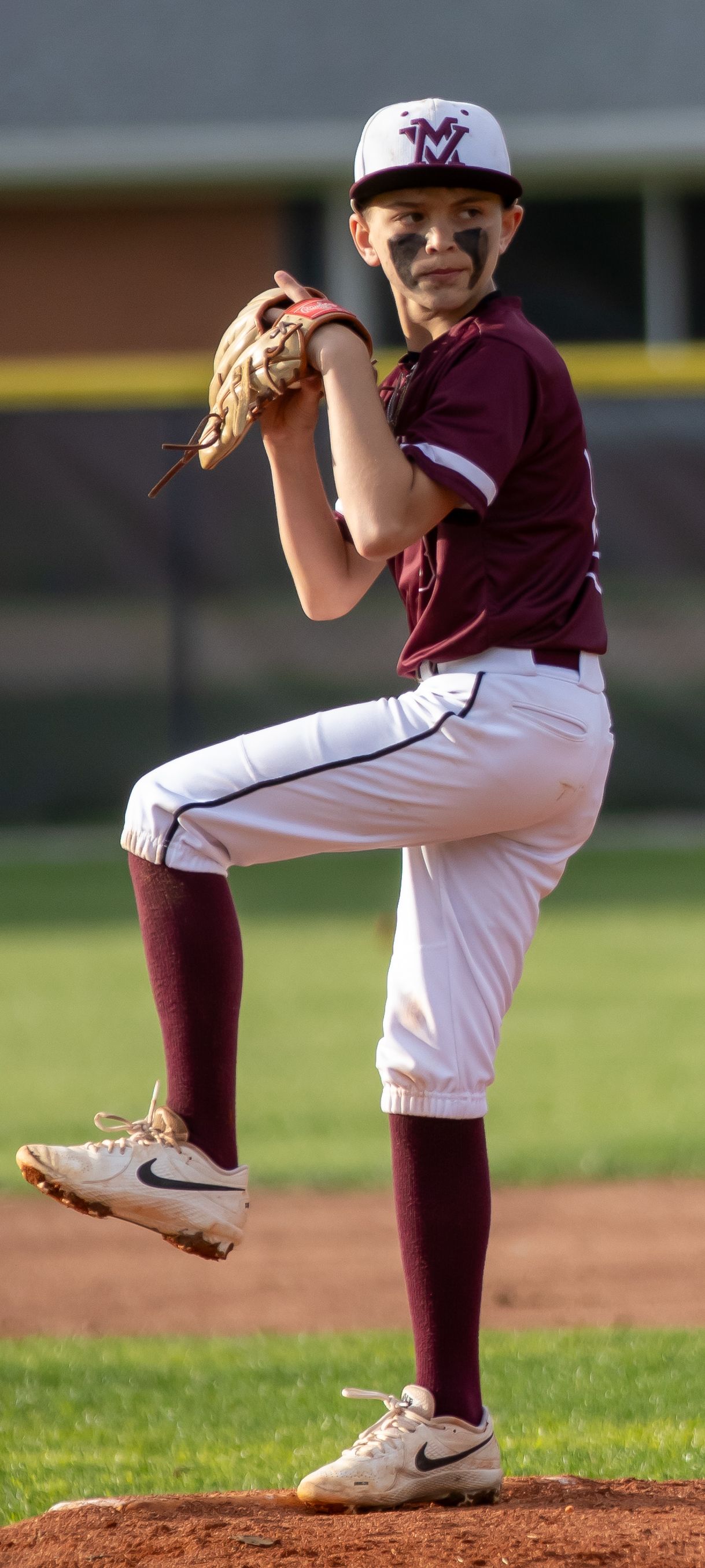 Young baseball pitcher in maroon Wildcats uniform in wind-up position on the mound.