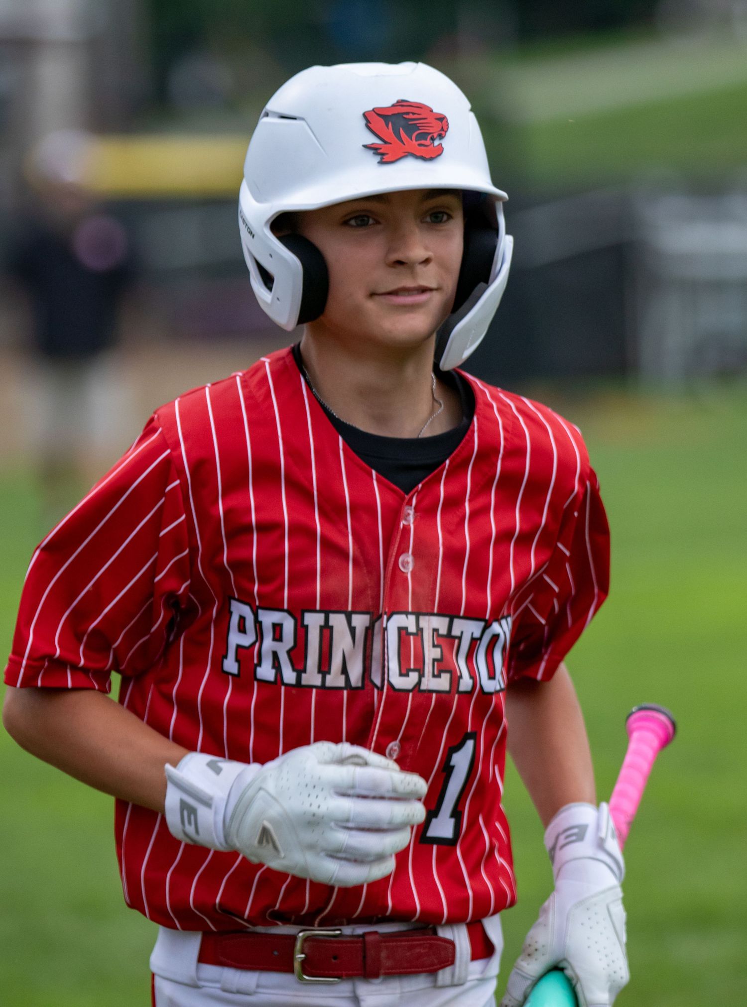 Young Princeton baseball player #1 in red pinstripe uniform holding bat at dugout.