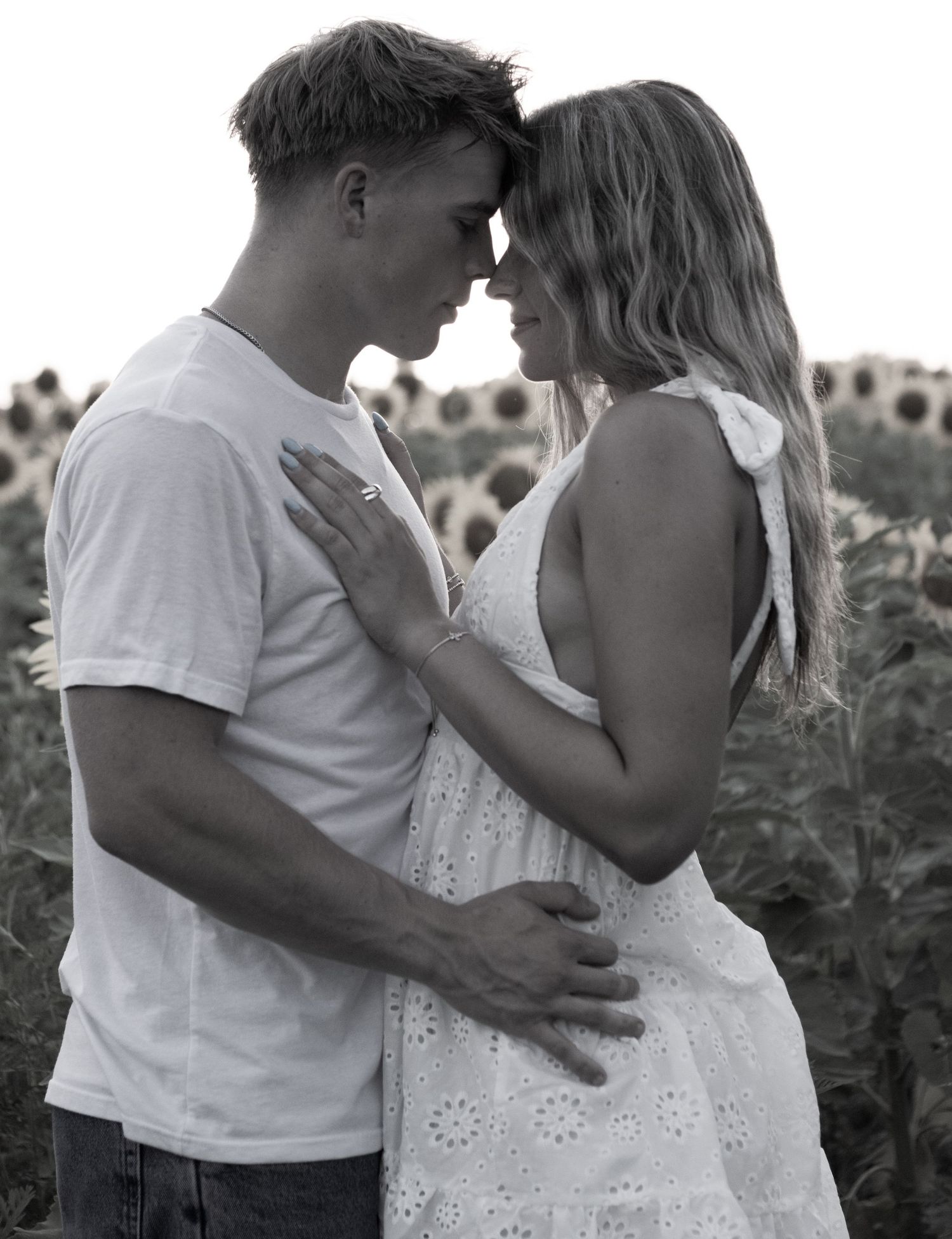 Black and white photo of romantic couple embracing forehead to forehead in a sunflower field.