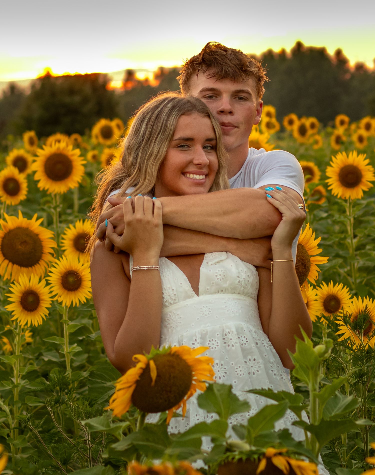 Happy couple embracing in vibrant sunflower field at golden sunset.