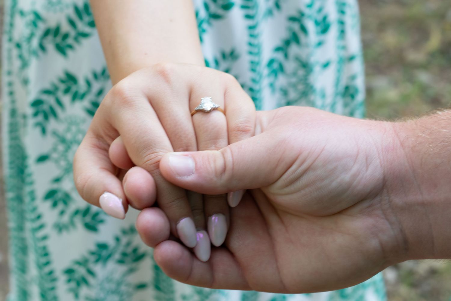 Close-up of couple holding hands with elegant engagement ring outdoors.