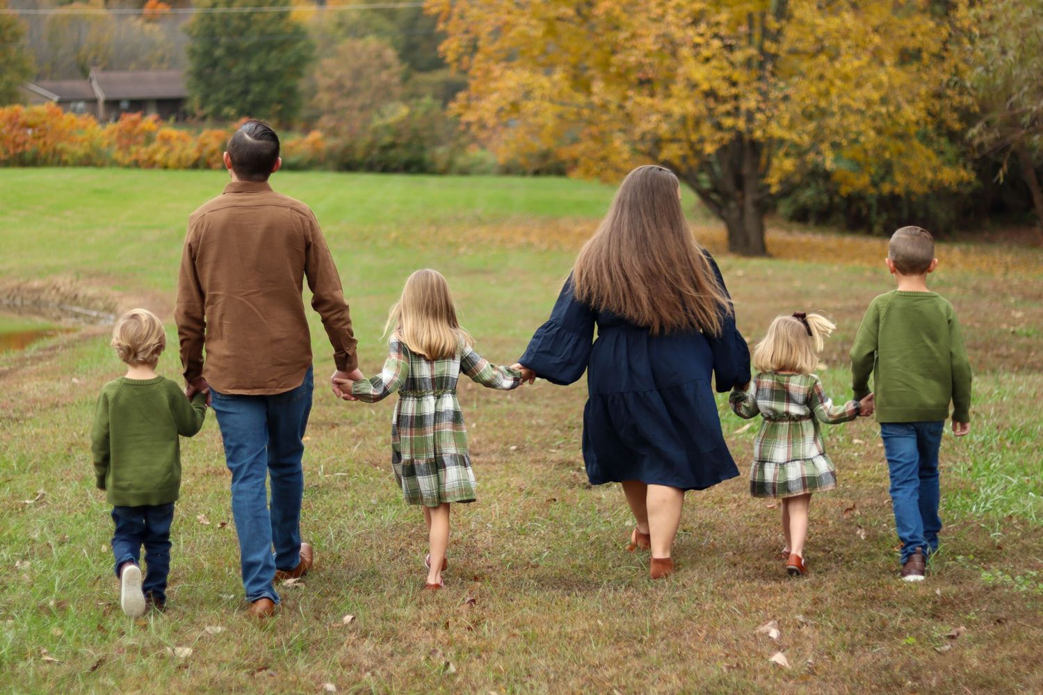 Family of six holding hands walking away through autumn park landscape.