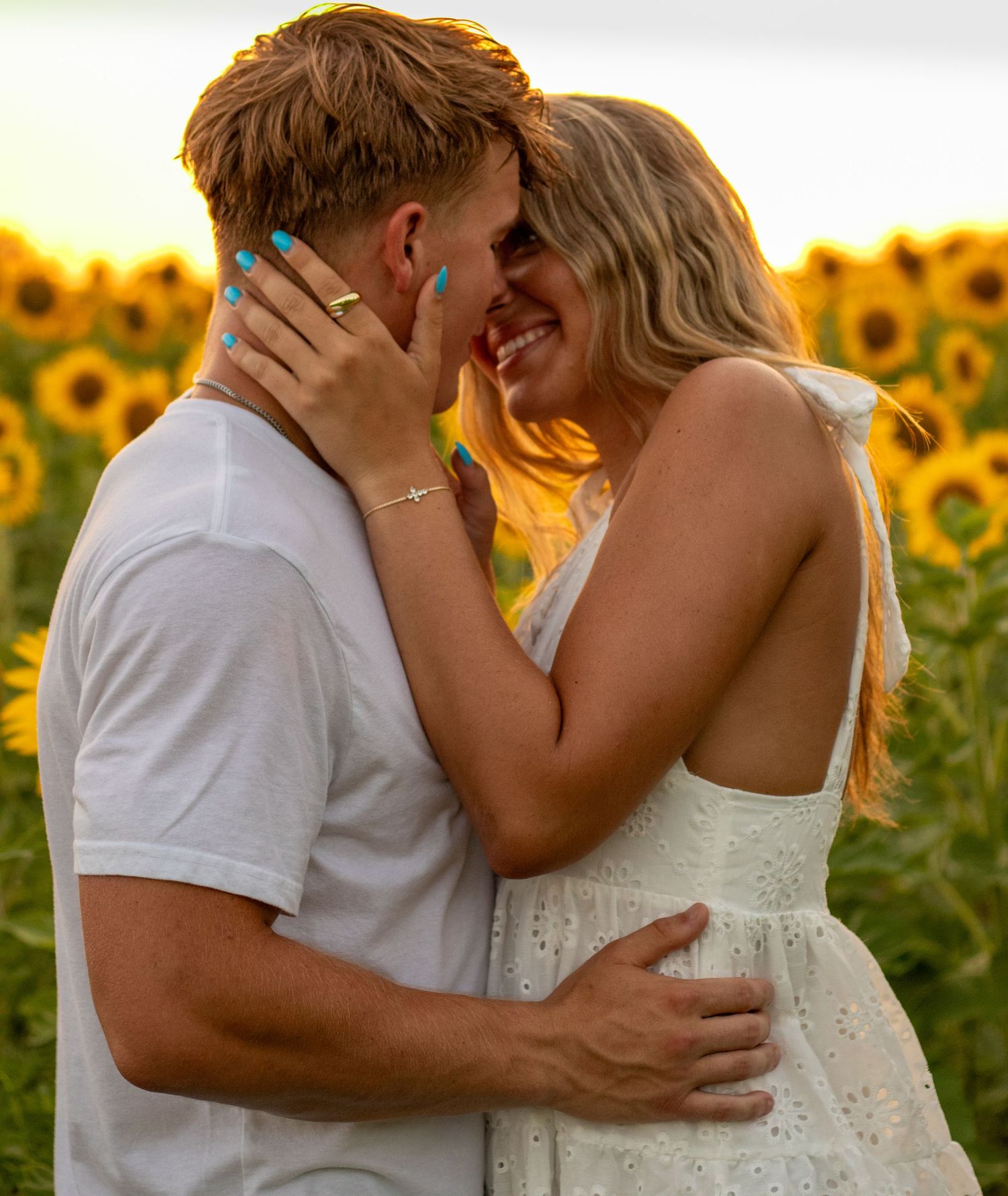 Smiling couple embracing closely in a golden sunflower field during a warm sunset.