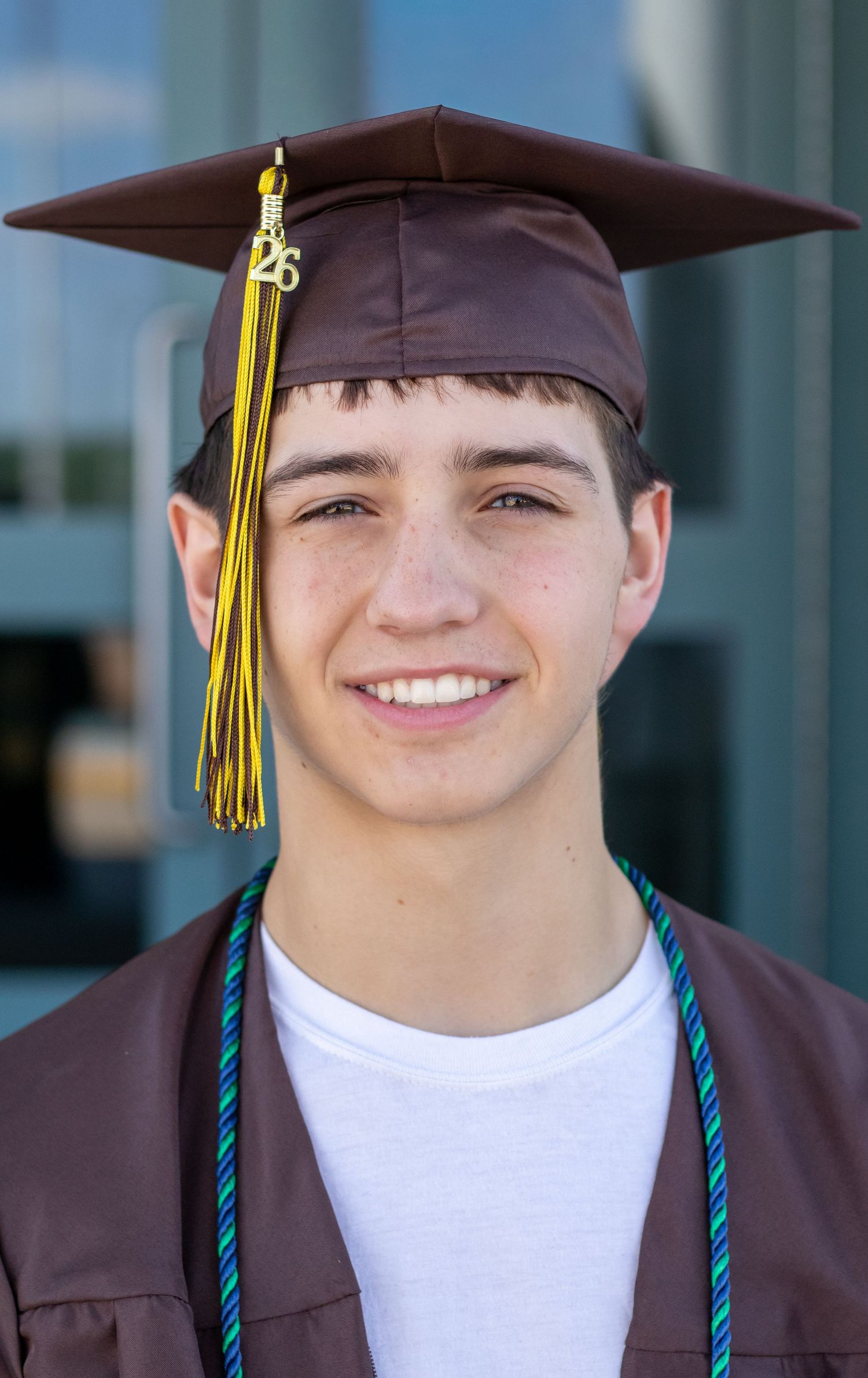 Smiling male high school graduate wearing brown mortarboard cap with yellow tassel portrait.