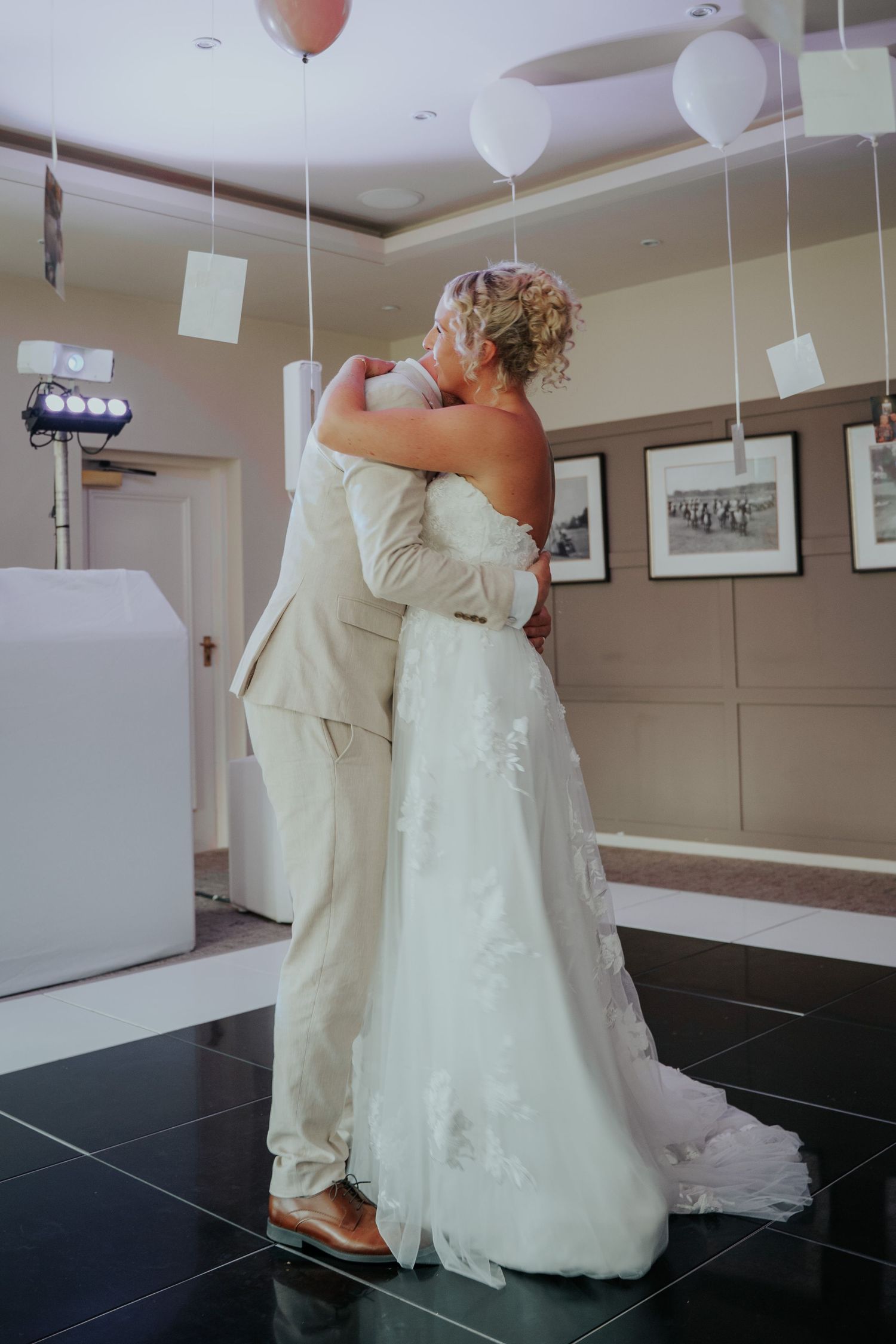 Newlyweds sharing first dance embrace under floating balloons in elegant wedding reception venue.