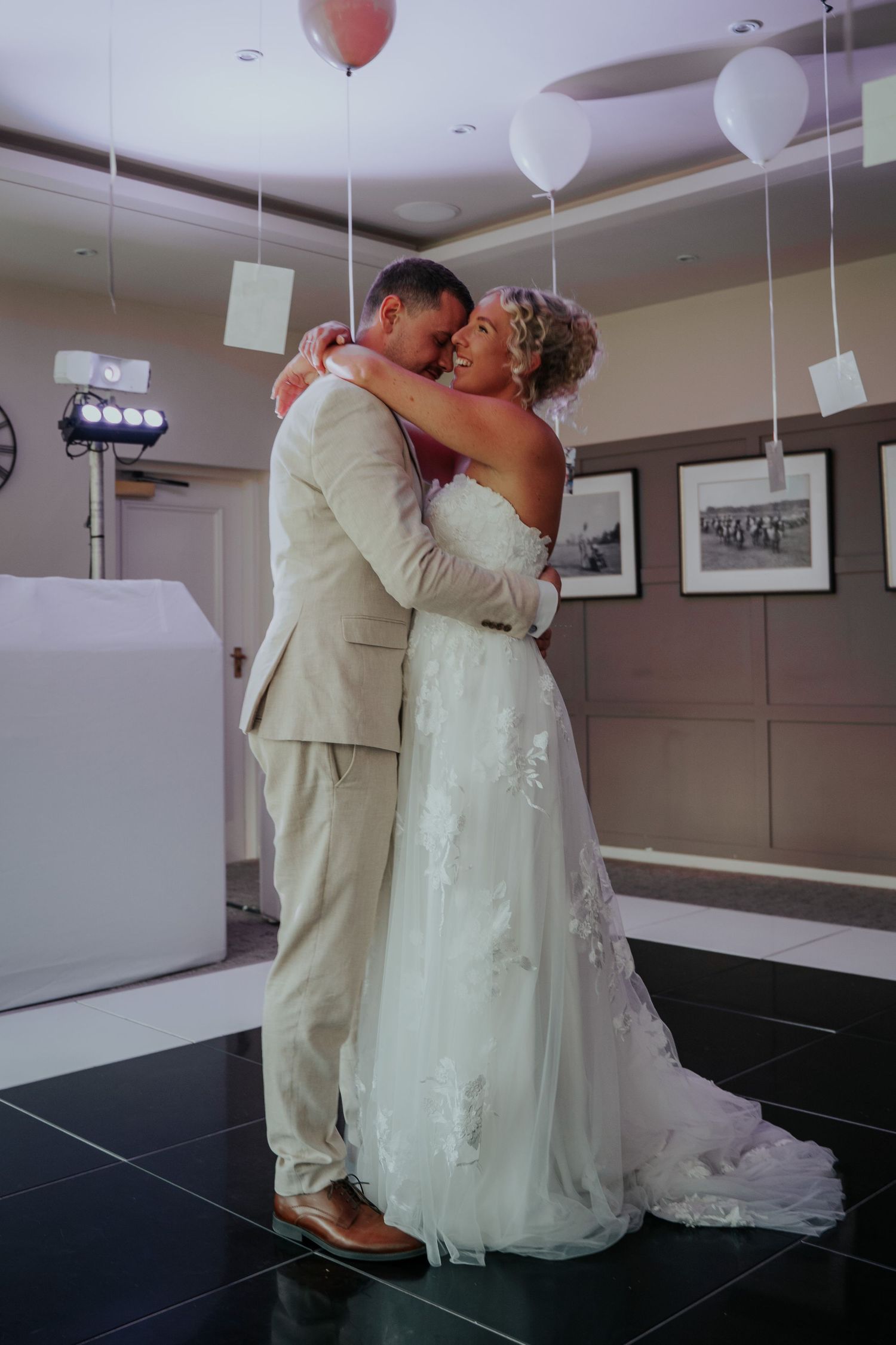 Bride and groom share first dance embrace in elegant wedding venue decorated with balloons.
